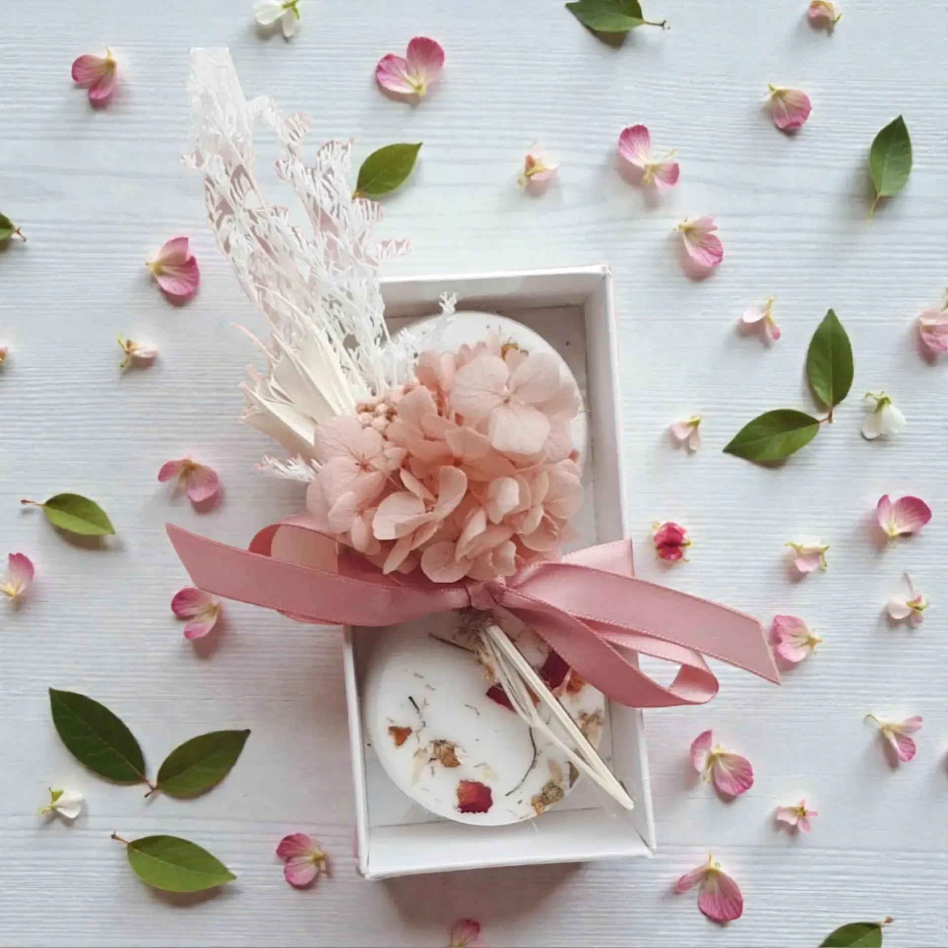 Two round, floral wax melts in a white box, decorated with pink ribbon and flowers.