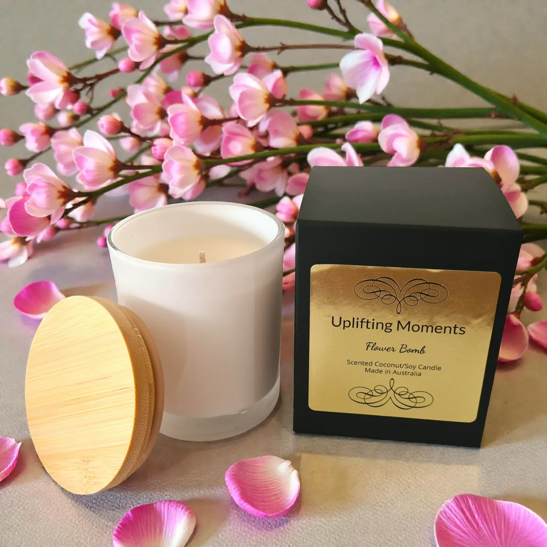 White candle in glass jar with wooden lid, surrounded by pink and cream roses on a silver surface.
