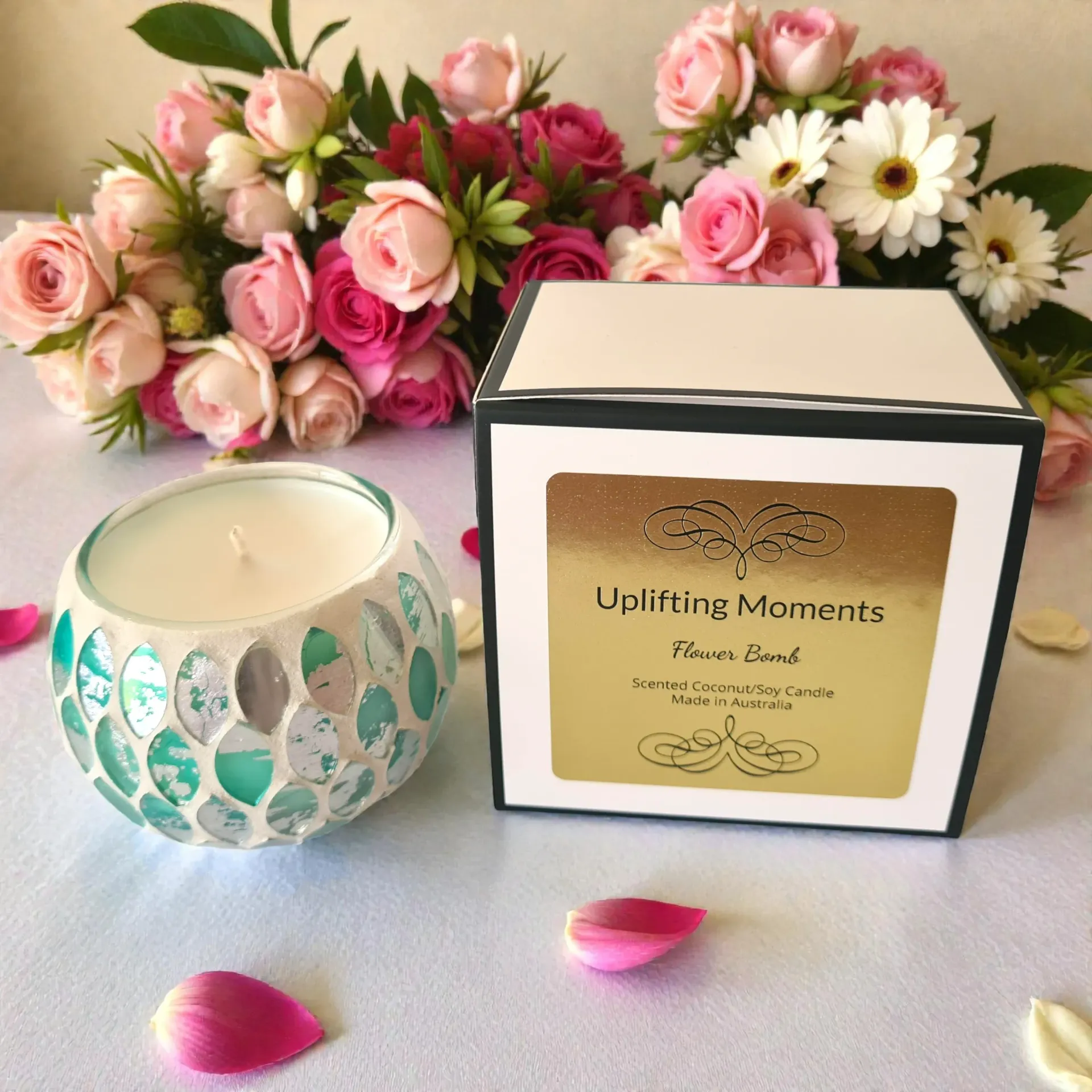 Glass candle holder with teal mosaic design, surrounded by pink and white flowers.