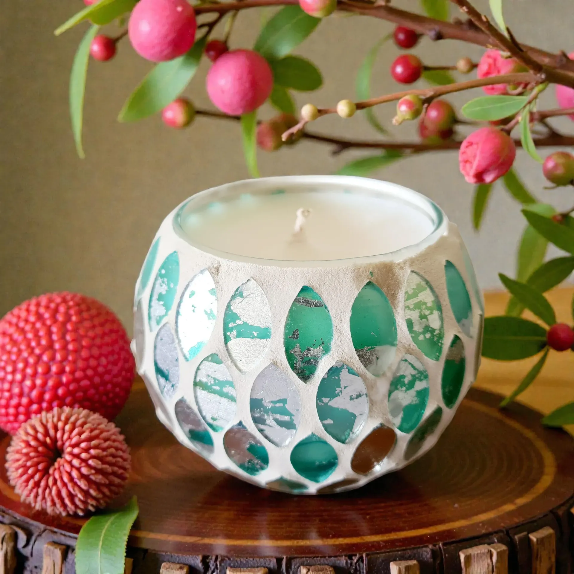 Mosaic glass candle in teal and silver, on a wooden coaster, with pink berries.