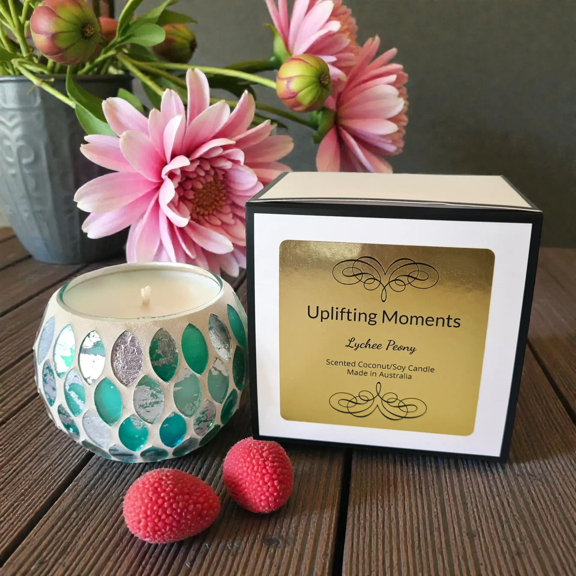 Mosaic glass candle in teal and silver, on a wooden coaster, with pink berries.