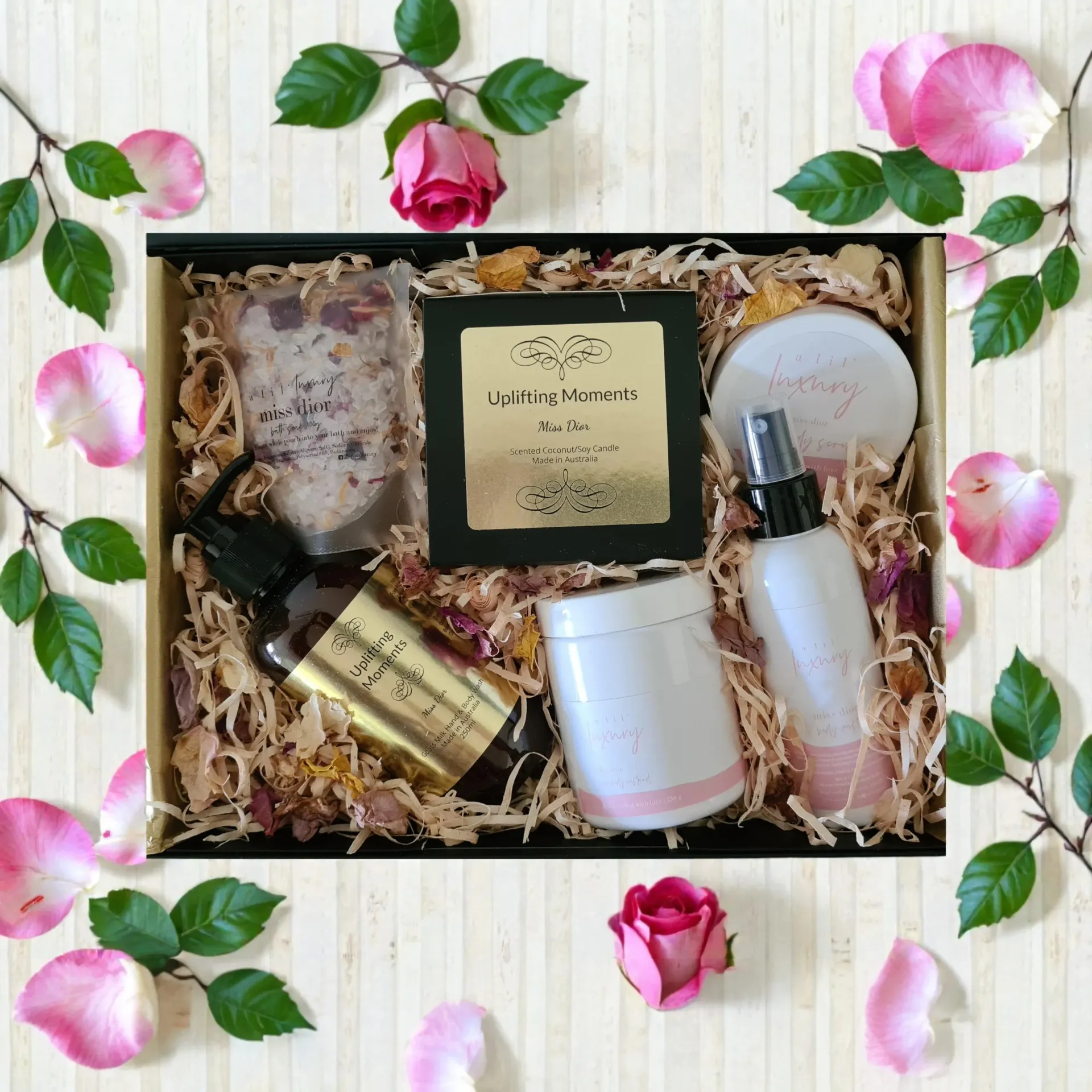 Gift box with rose-themed bath products, surrounded by petals, leaves, and roses.