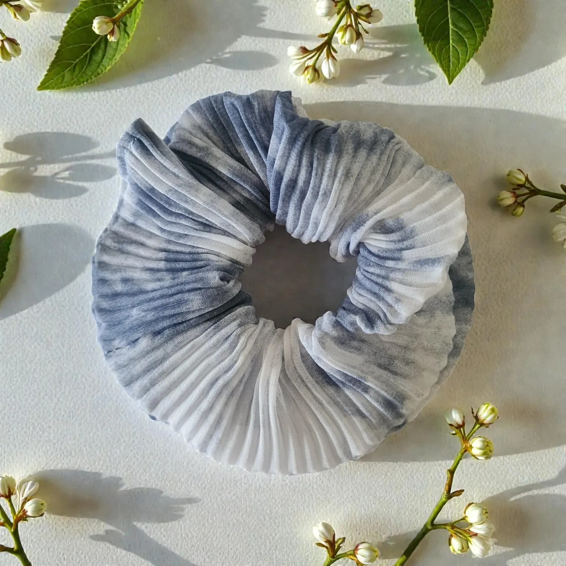 Blue and white pleated scrunchie with flowers on a white surface.