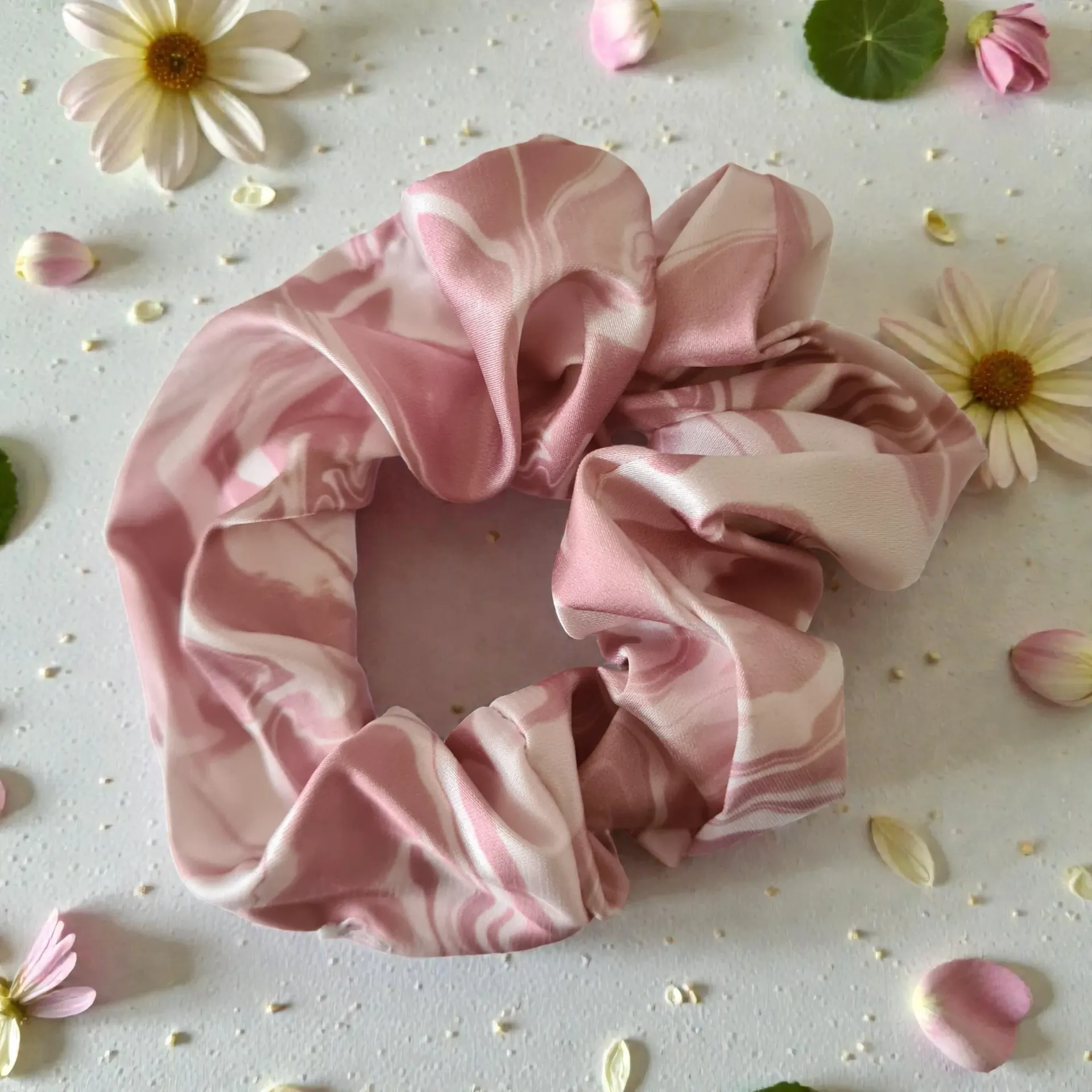 Pink and white marbled scrunchie on a white surface with flowers and petals.