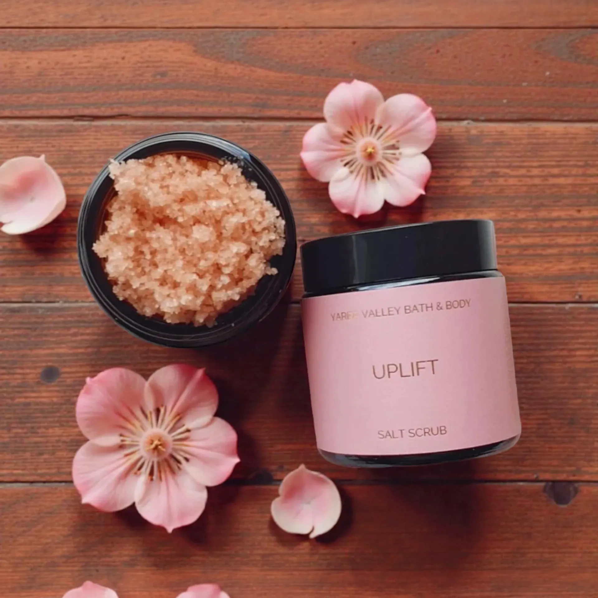 Salt scrub jar and bowl, pink flowers, on a wooden surface.