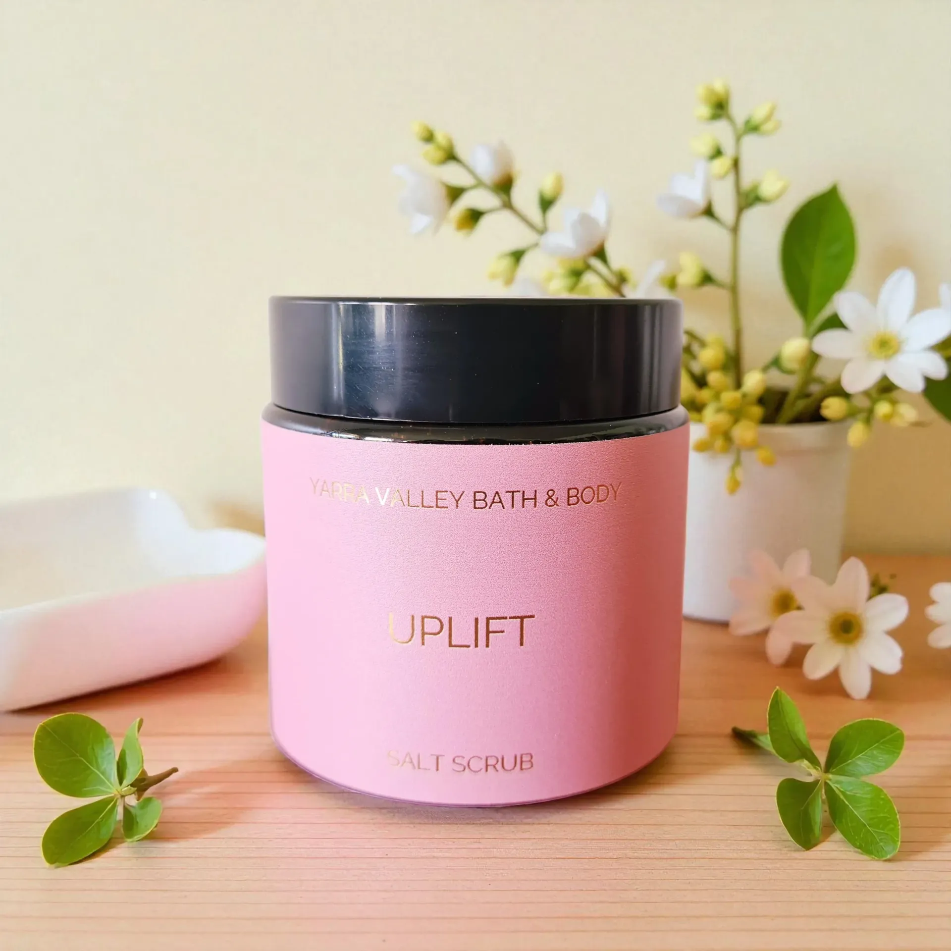 Salt scrub jar and bowl, pink flowers, on a wooden surface.