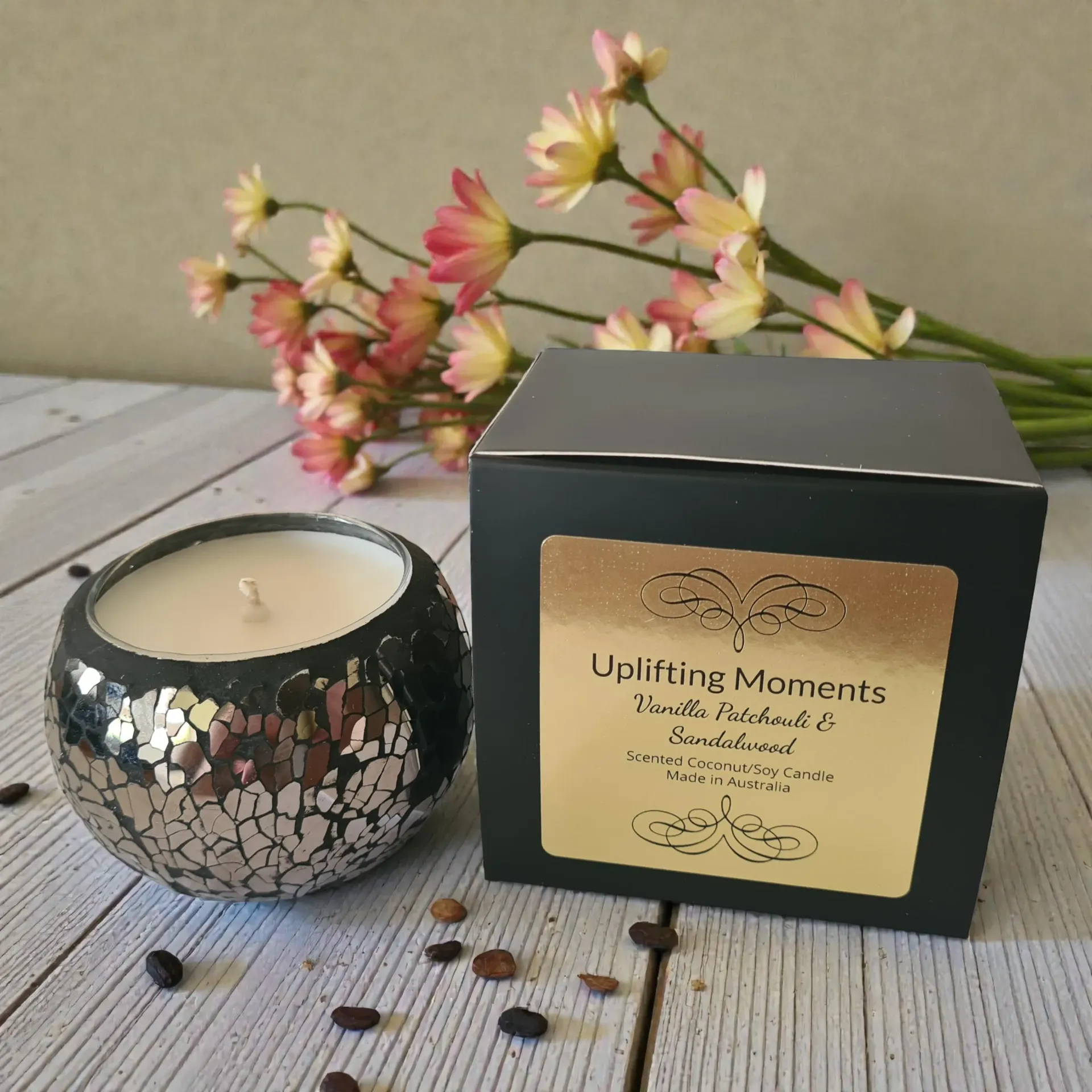 Silver mosaic candle with white wax, flowers, and wooden accents on a wooden surface.