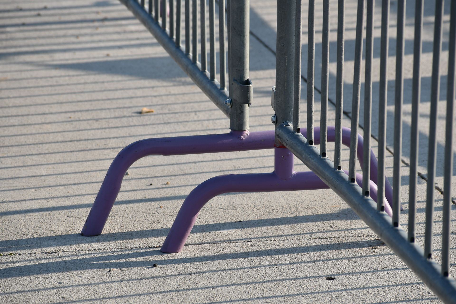 Purple-footed metal barrier on a concrete surface, casting a shadow.