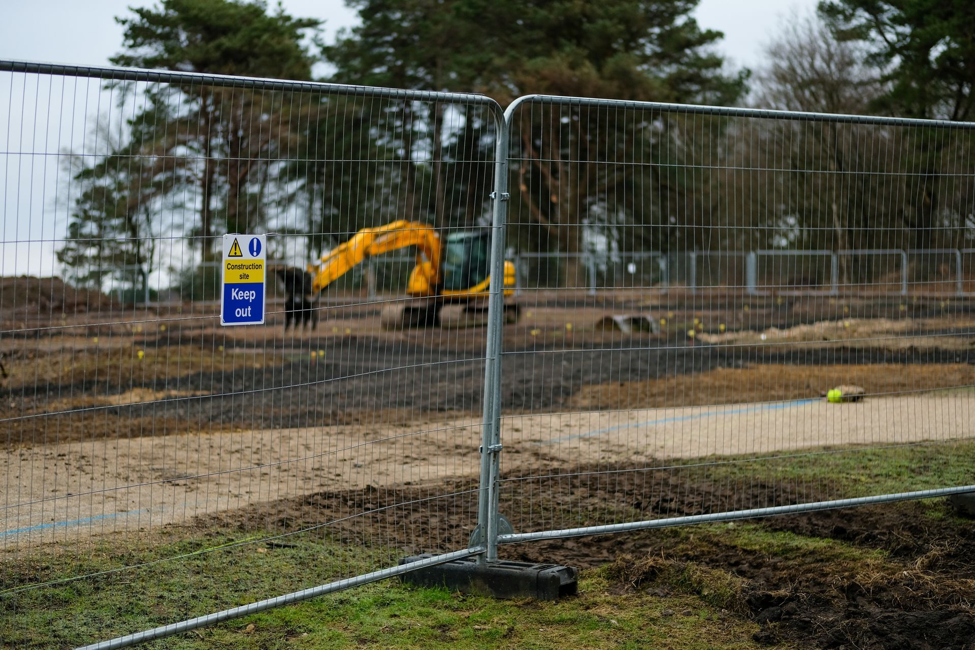 Temporary metal fencing surrounds an active construction site with heavy equipment.