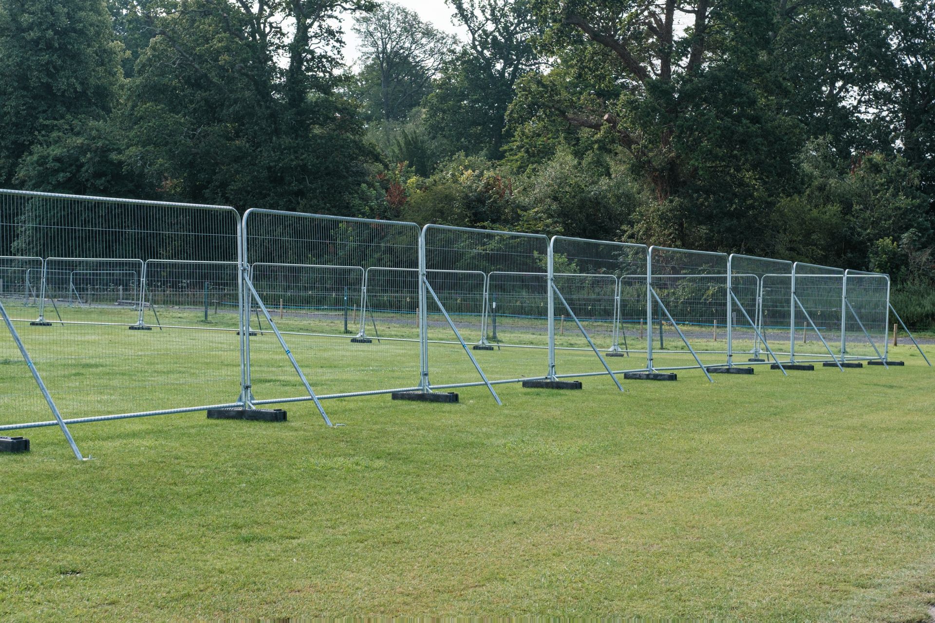 Metal crowd control barriers on a grassy field, trees in the background. Metal crowd control barriers on a grassy field, trees in the background.