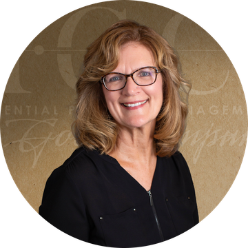 Woman with glasses smiling, wearing a black shirt, in front of a brown backdrop.