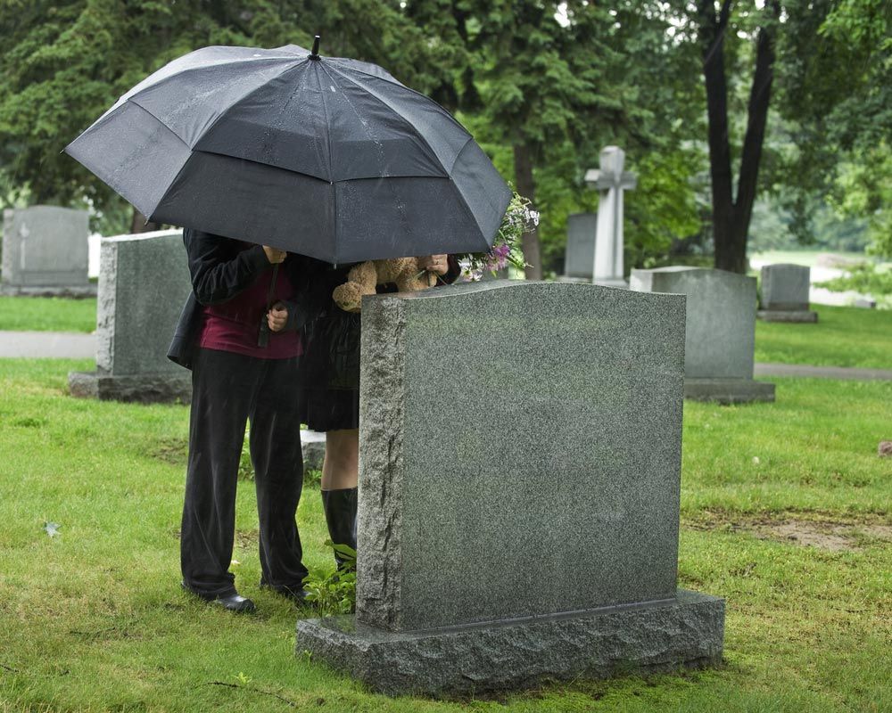 Two Young People Under An Umbrella Bringing A Teddy Bear And Flowers To A Grave Site In Funeral — Trusted Funeral Directors in Sydney, NSW