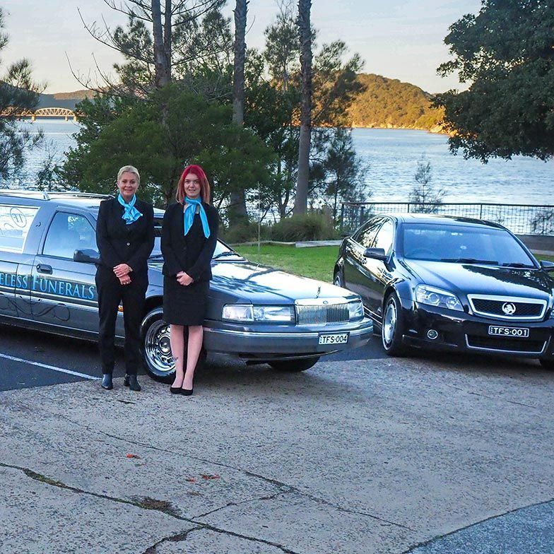 Two Women Team Standing In Front Of Hearses — Trusted Funeral Directors in The Entrance, NSW