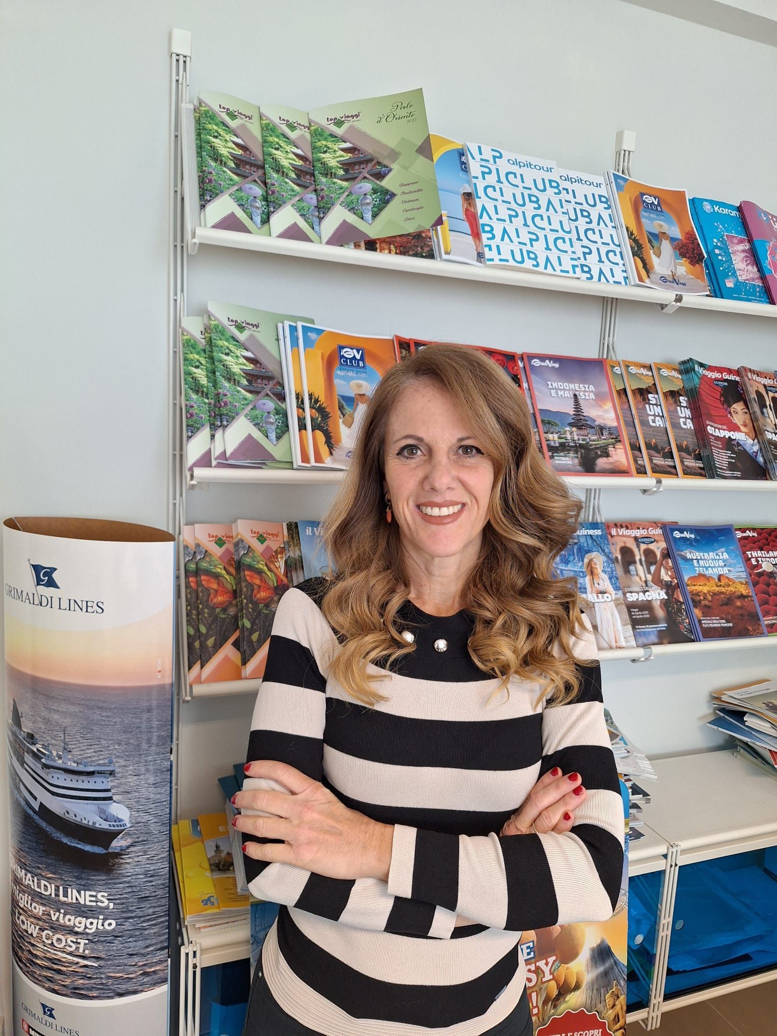 Interno dell'agenzia di viaggi Laura Gibaldi Travel: brochure sugli scaffali, scrivania con computer, pubblicità di Abu Dhabi, foto delle piramidi.