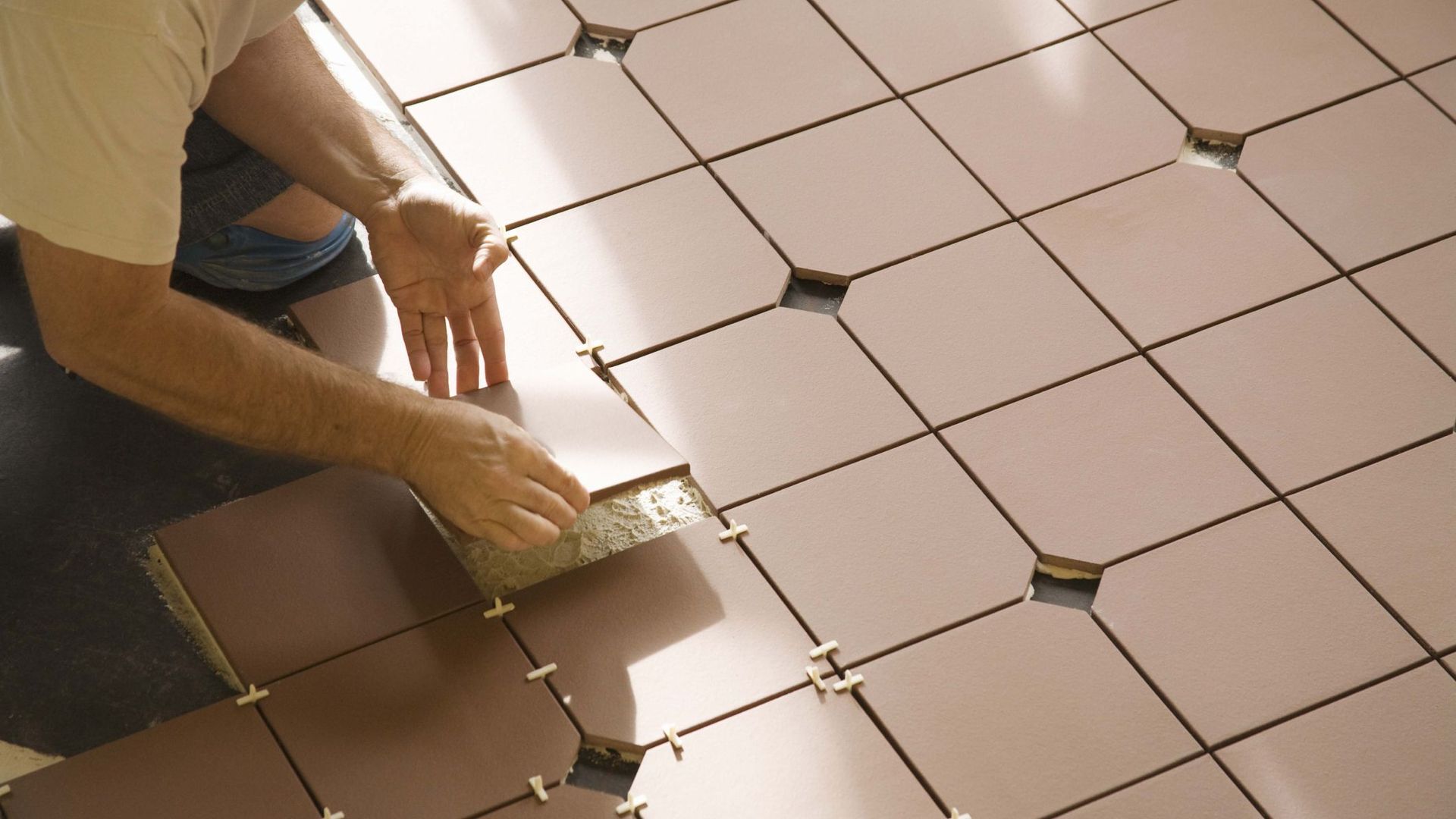 a man is installing tiles on a wall in a bathroom .