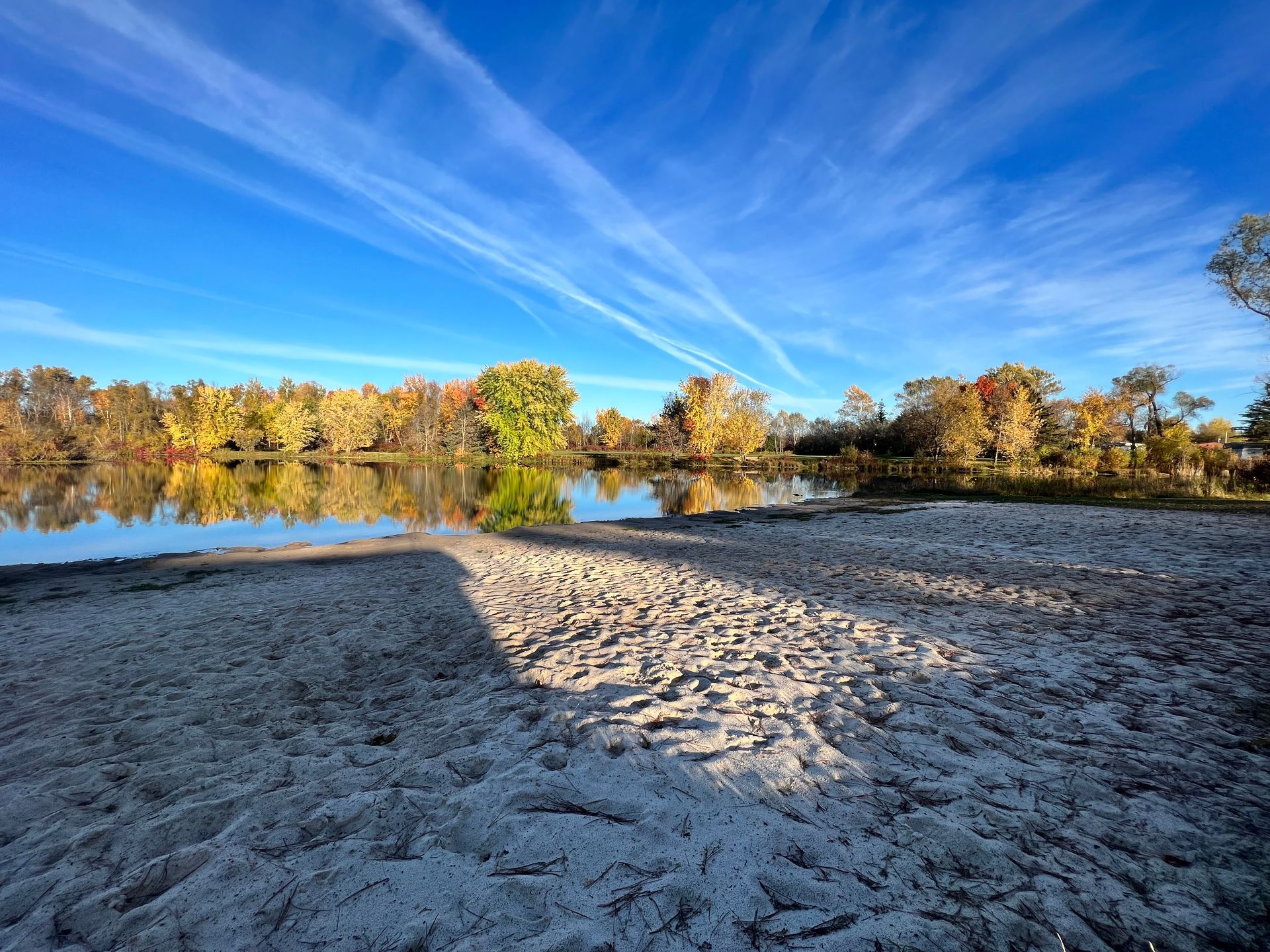 A sandy beach next to a lake with trees in the background on a sunny day.