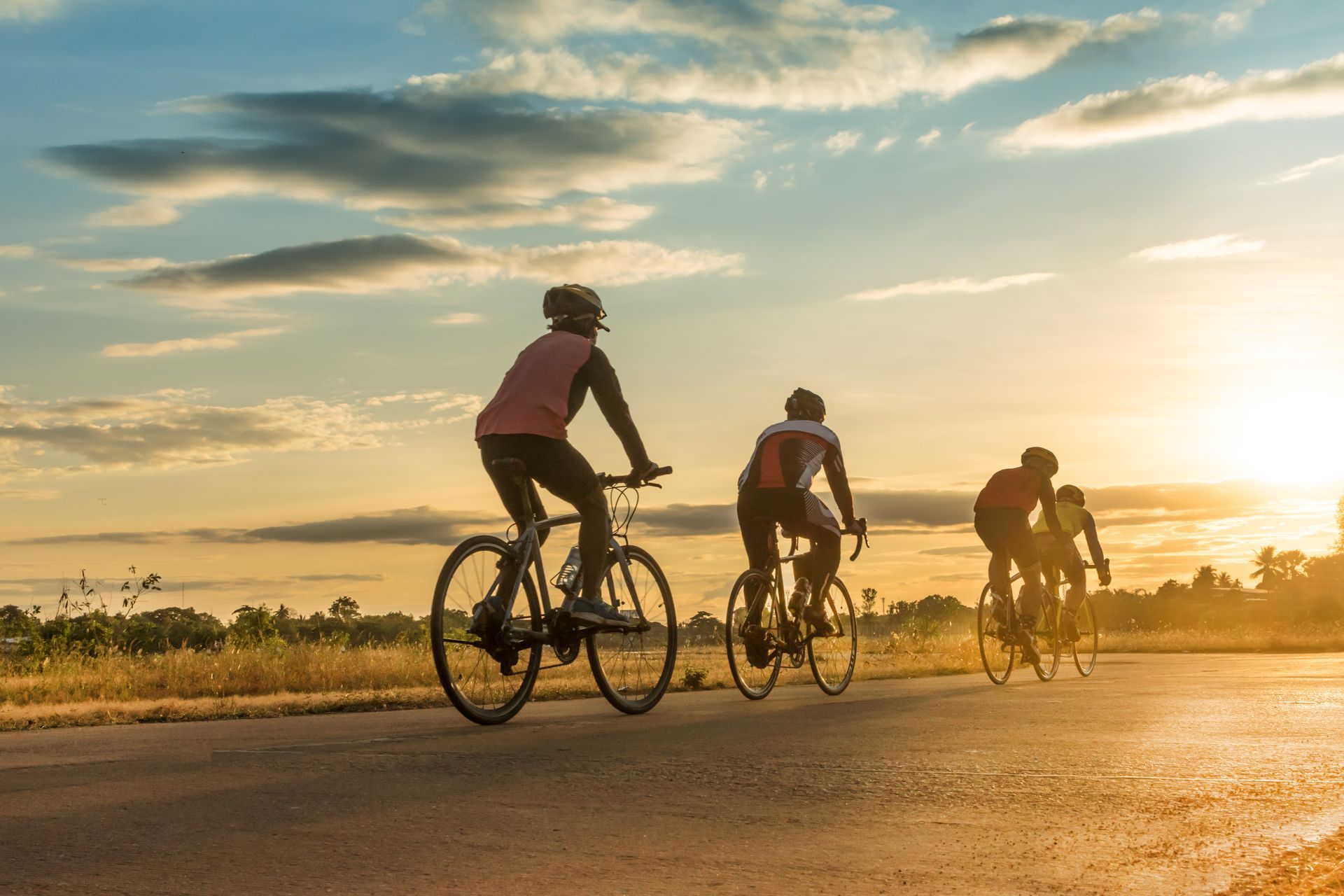 A group of people are riding bicycles down a road at sunset.