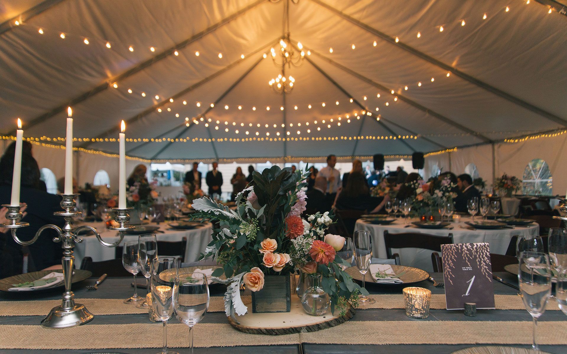 A tent is being set up for a wedding reception with tables and candles.
