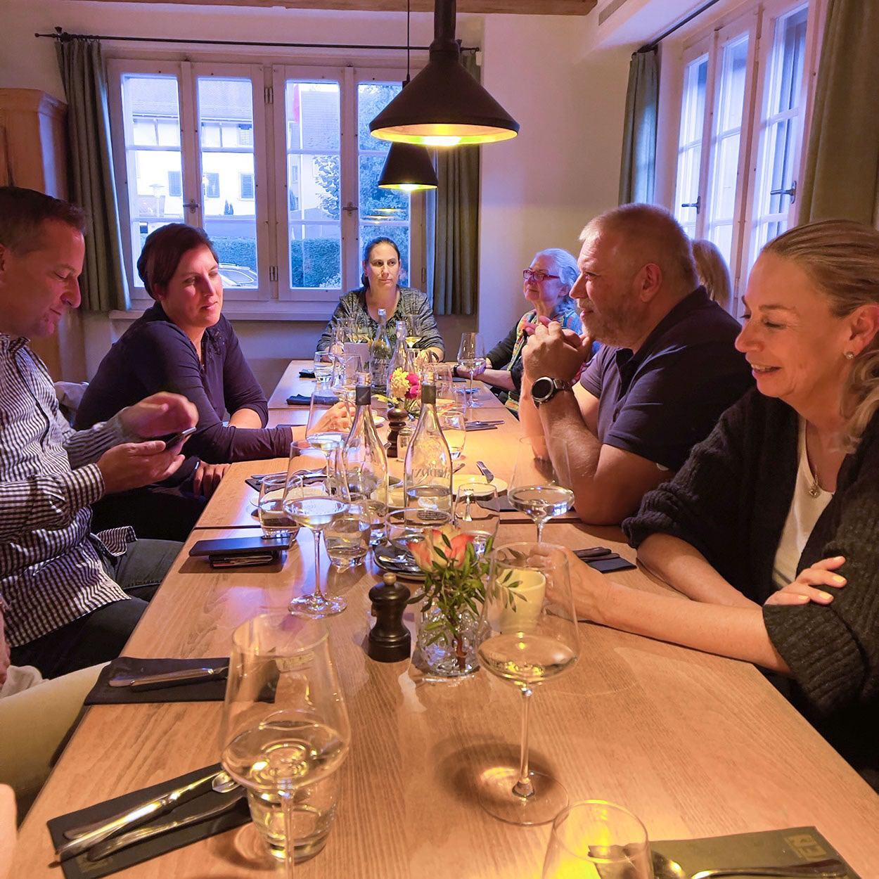 Eine Gruppe von Menschen sitzt mit Weingläsern an einem langen Tisch.