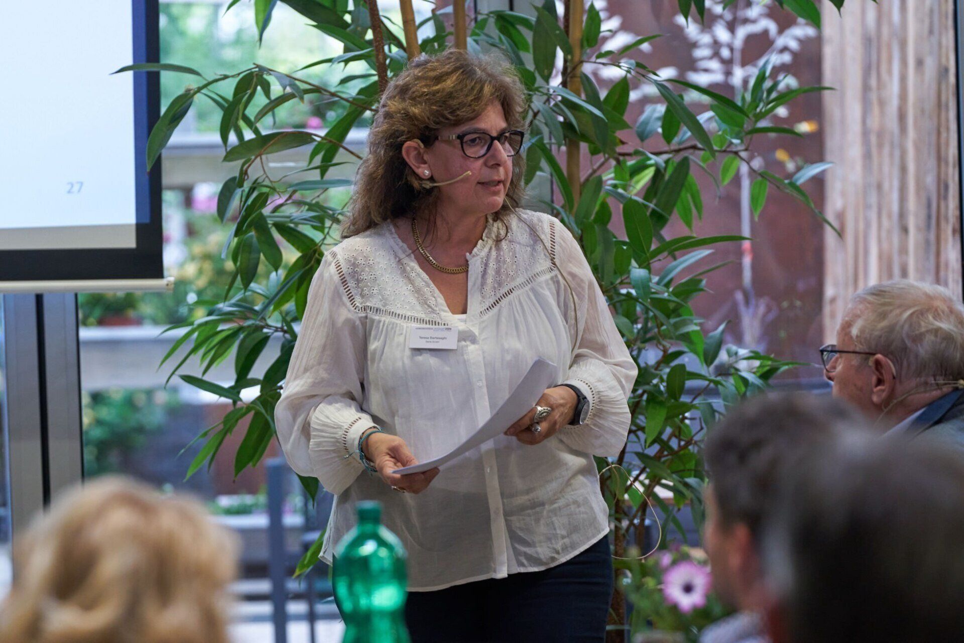 Eine Frau steht vor einer Gruppe von Menschen und hält ein Stück Papier in der Hand.
