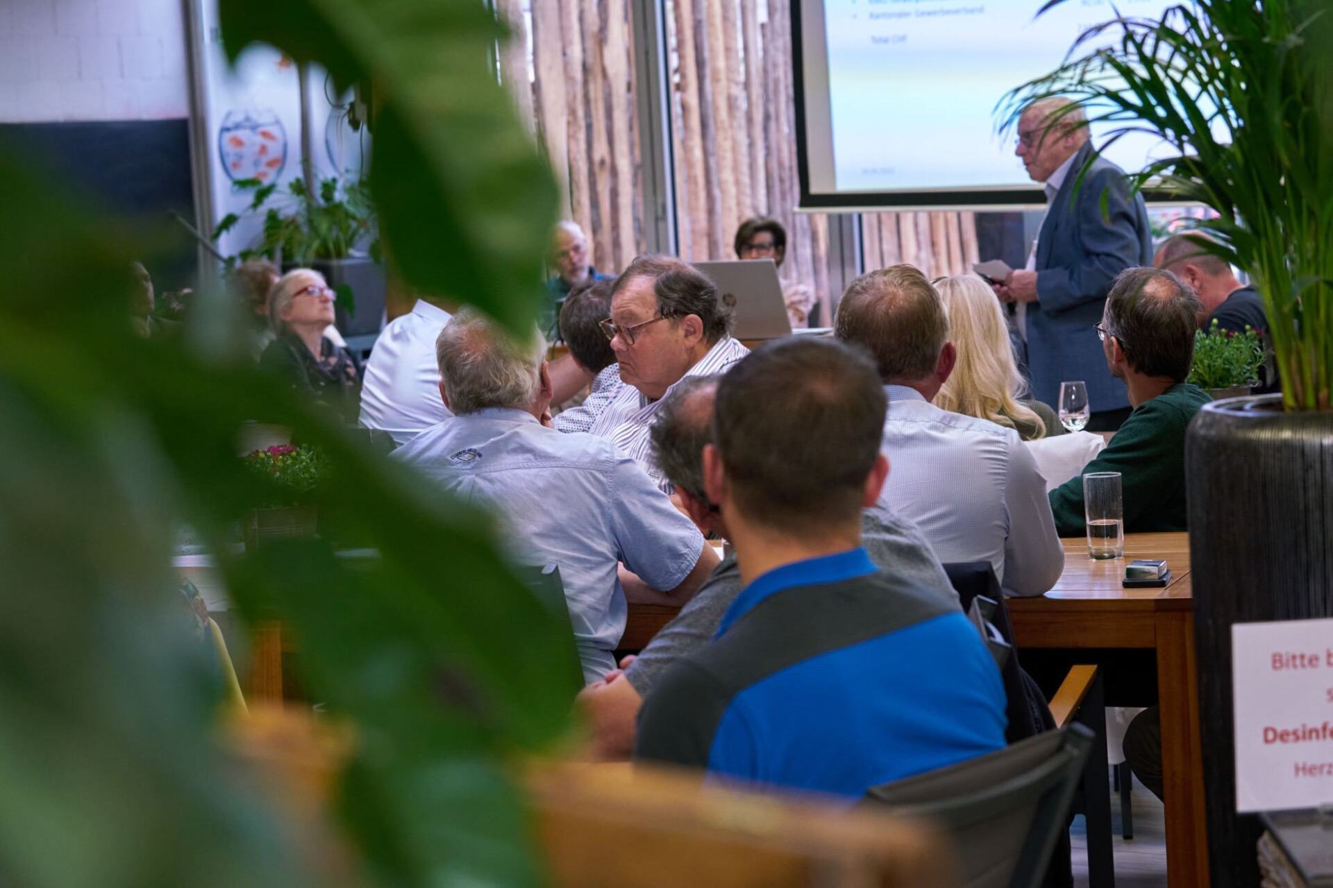 Eine Gruppe von Leuten sitzt in einem Raum und sieht sich eine Präsentation an.