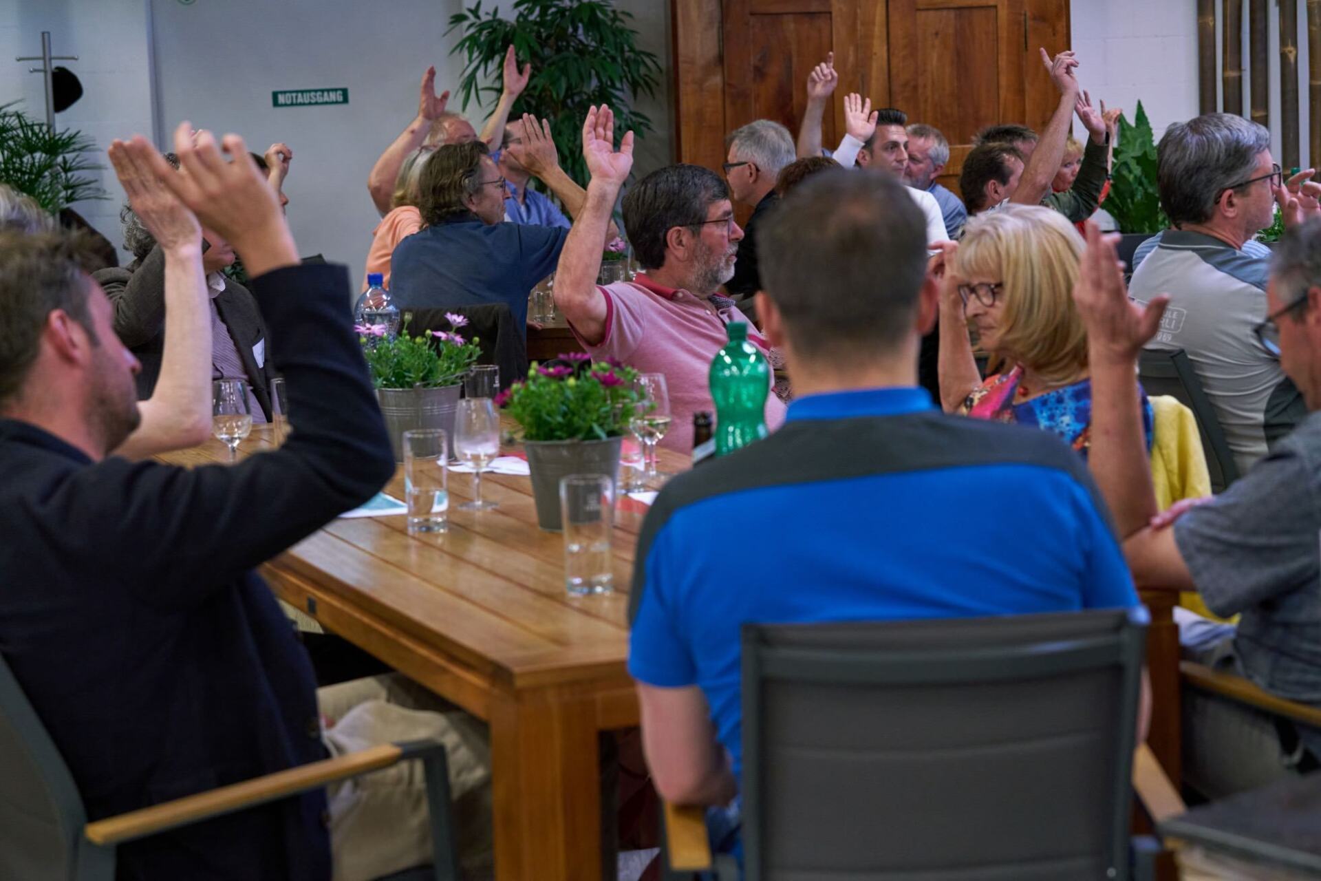 Eine Gruppe von Leuten sitzt mit erhobenen Händen an einem Tisch.