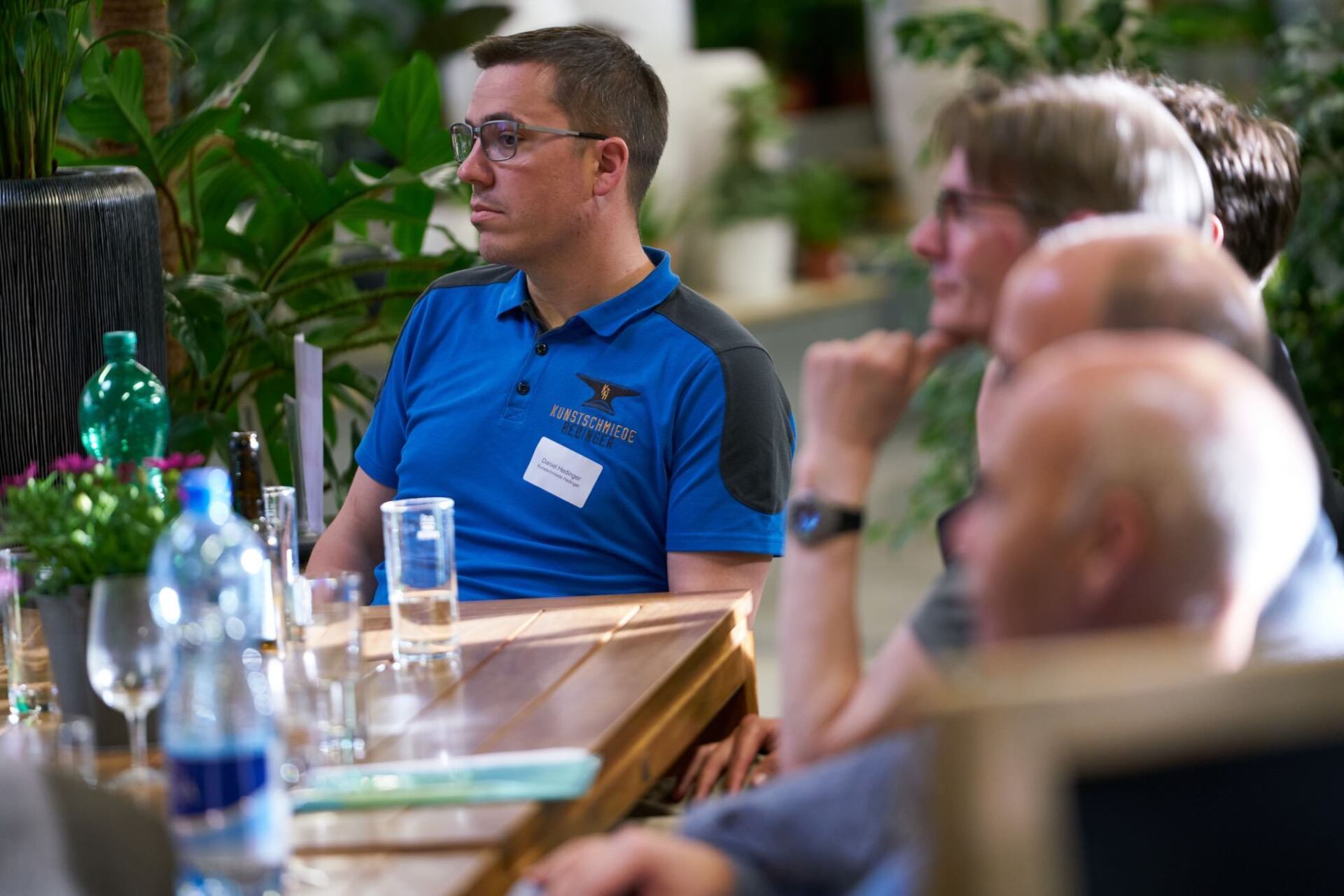 Ein Mann in einem blauen Hemd sitzt mit anderen Leuten an einem Tisch.