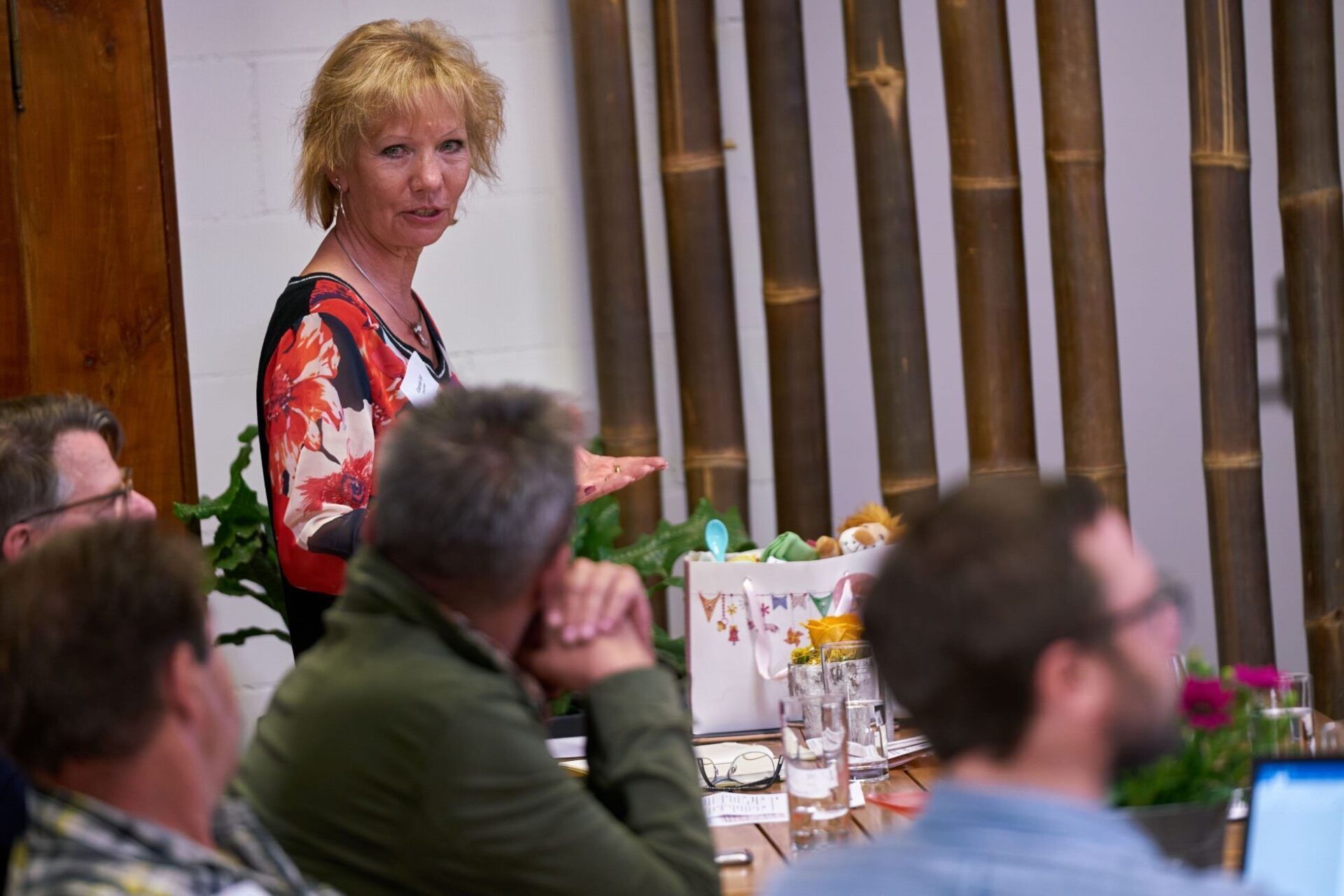 Eine Frau hält vor einer Gruppe von Leuten, die an einem Tisch sitzen, eine Präsentation.