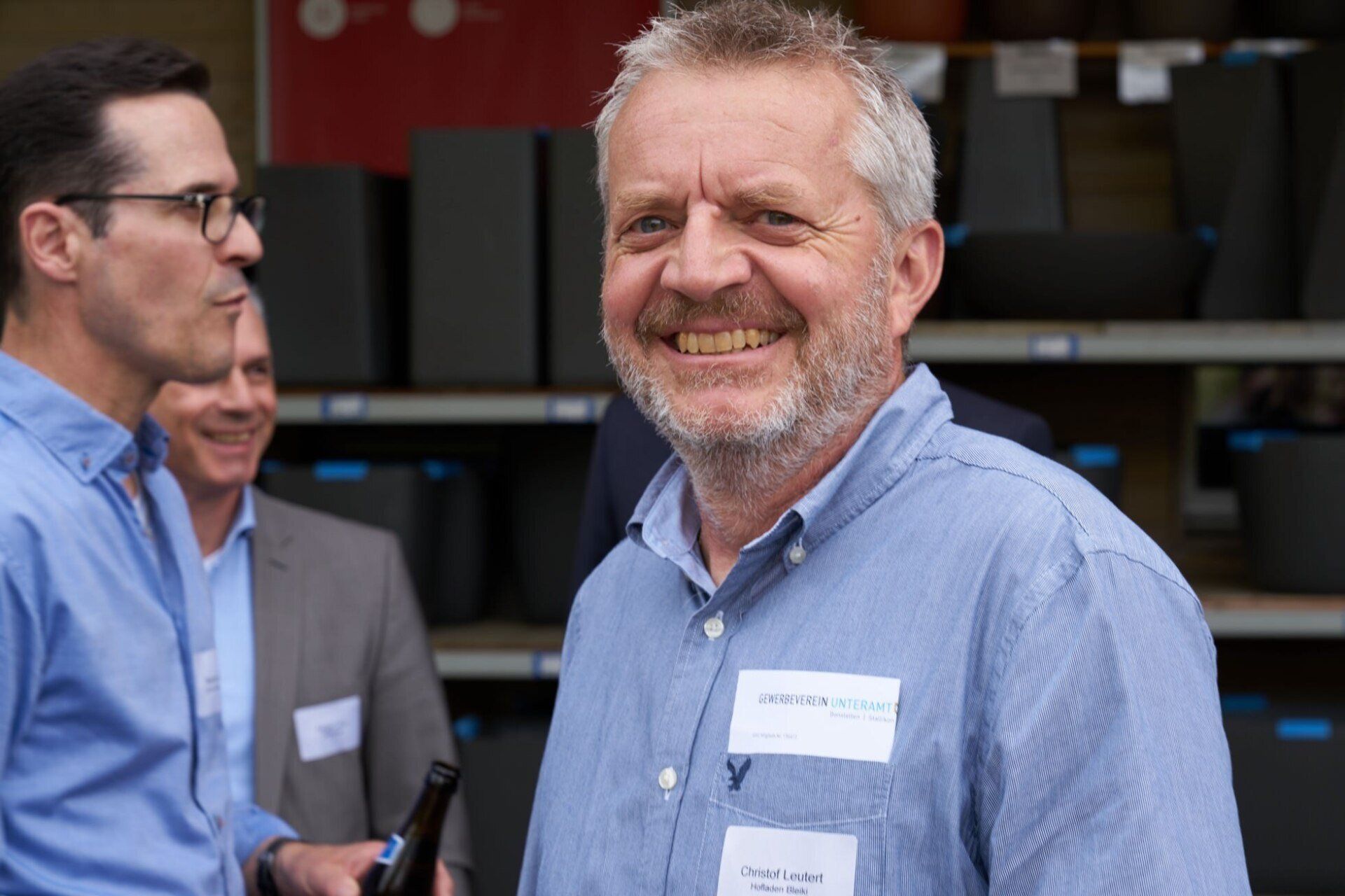 Ein Mann mit Bart lächelt und hält eine Flasche Bier in der Hand.