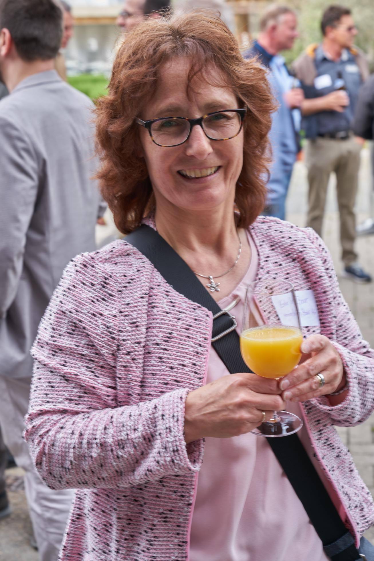 Eine Frau in einer rosa Jacke hält ein Glas Orangensaft.