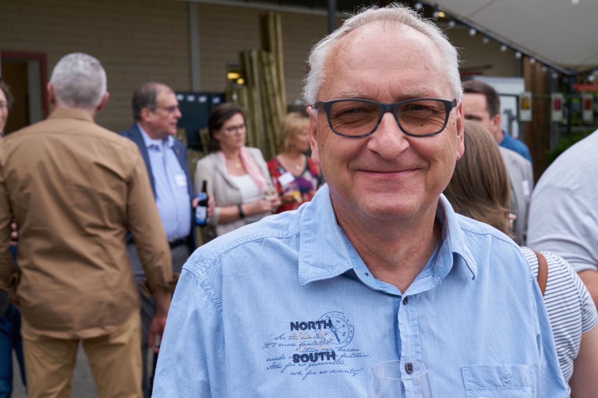 Ein Mann mit Brille und blauem Hemd steht in einer Menschenmenge.