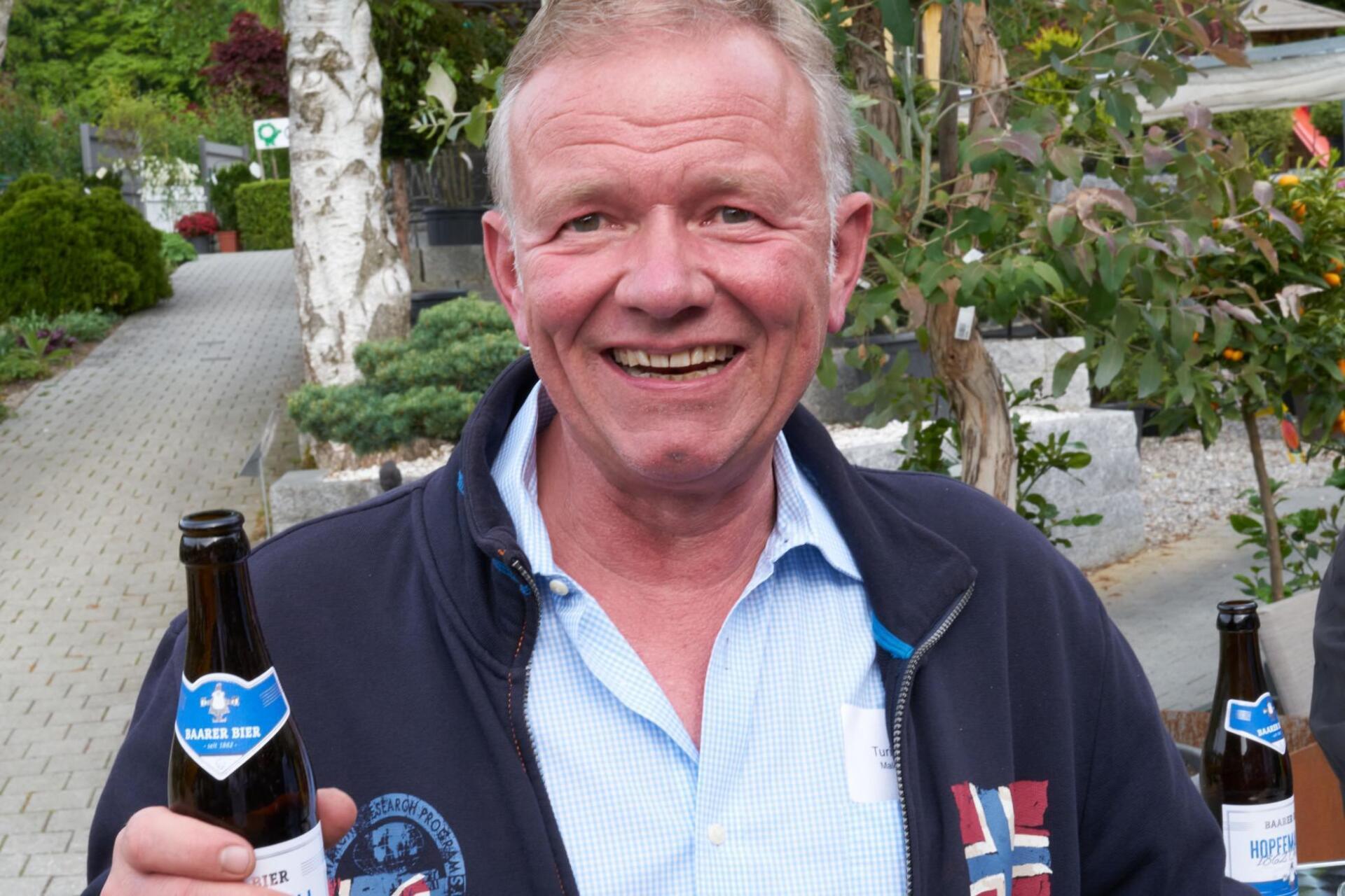 Ein Mann in einem blauen Hemd hält zwei Flaschen Bier