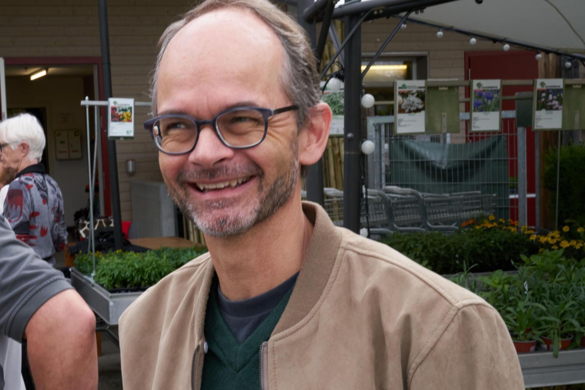Ein Mann mit Brille und brauner Jacke lächelt.
