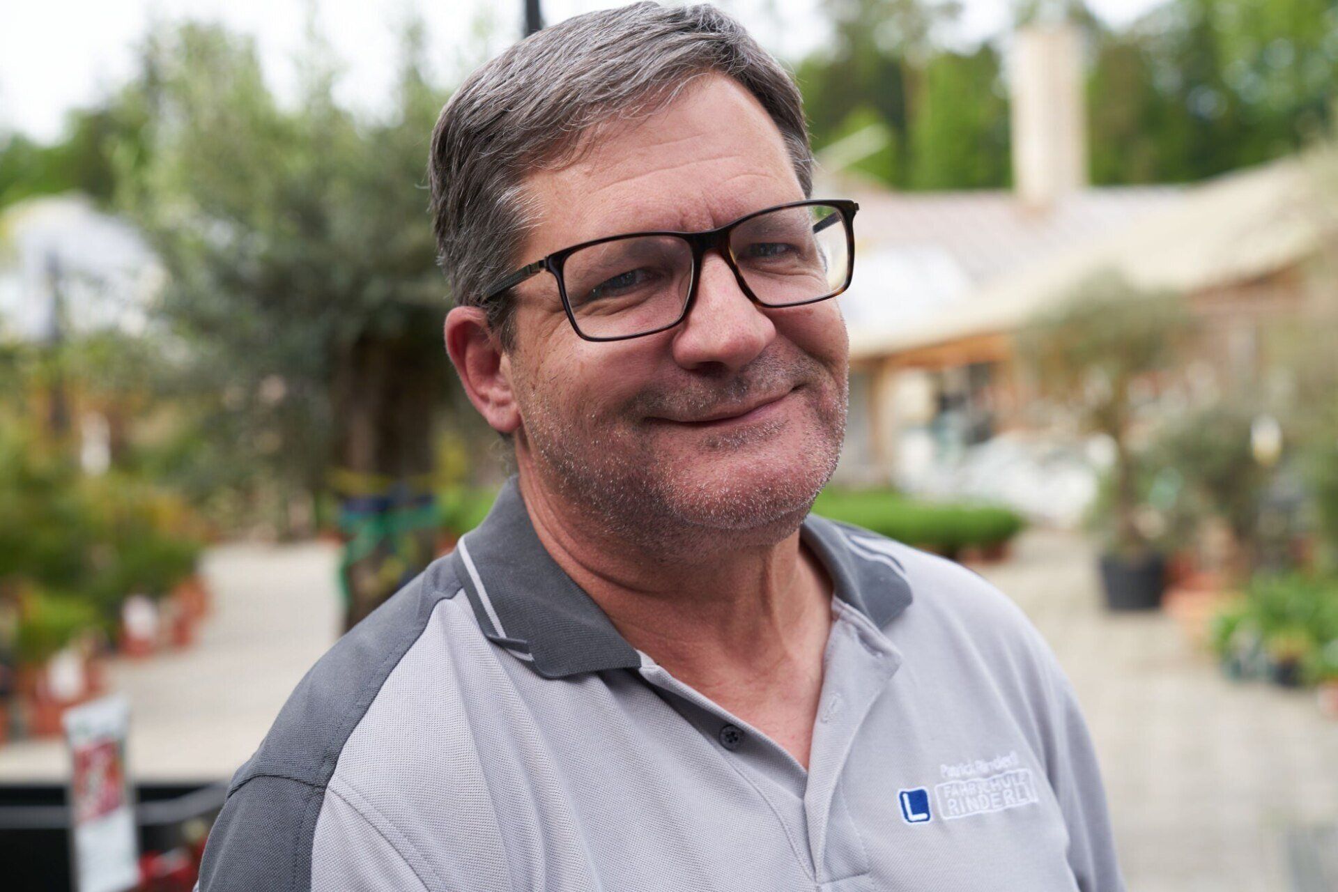 Ein Mann mit Brille und grauem Hemd lächelt.