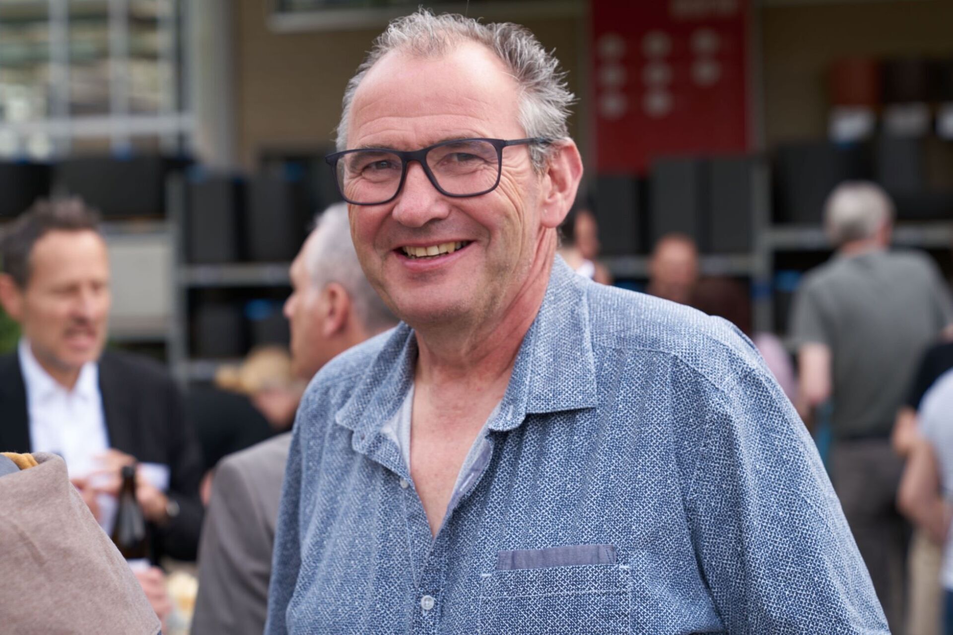 Ein Mann mit Brille und blauem Hemd lächelt in die Kamera.