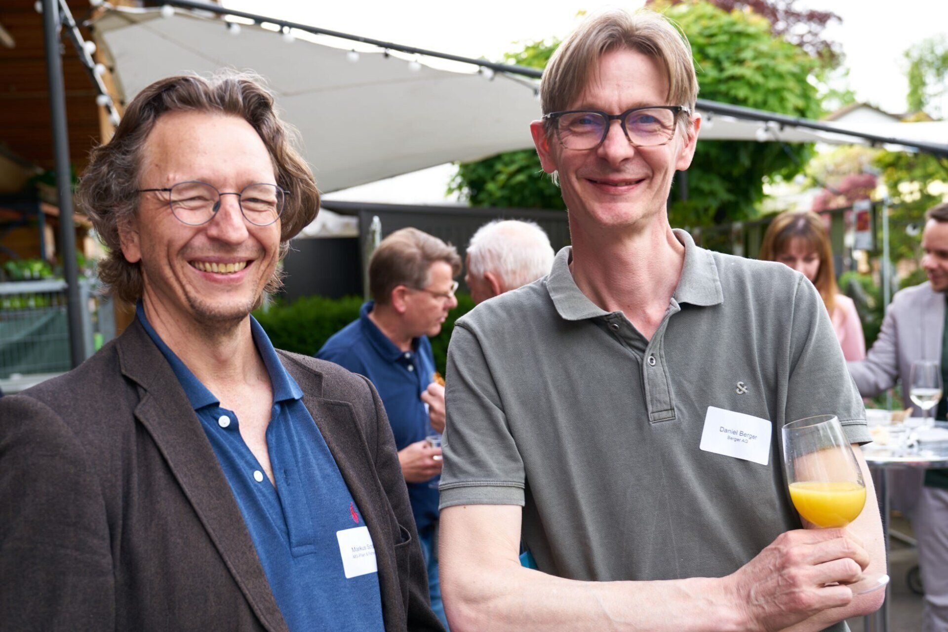 Zwei Männer stehen nebeneinander und einer hält ein Glas Orangensaft.