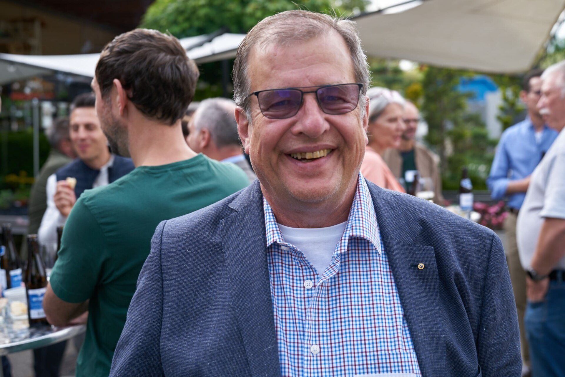 Ein Mann mit Brille und Anzug lächelt in einer Menschenmenge.