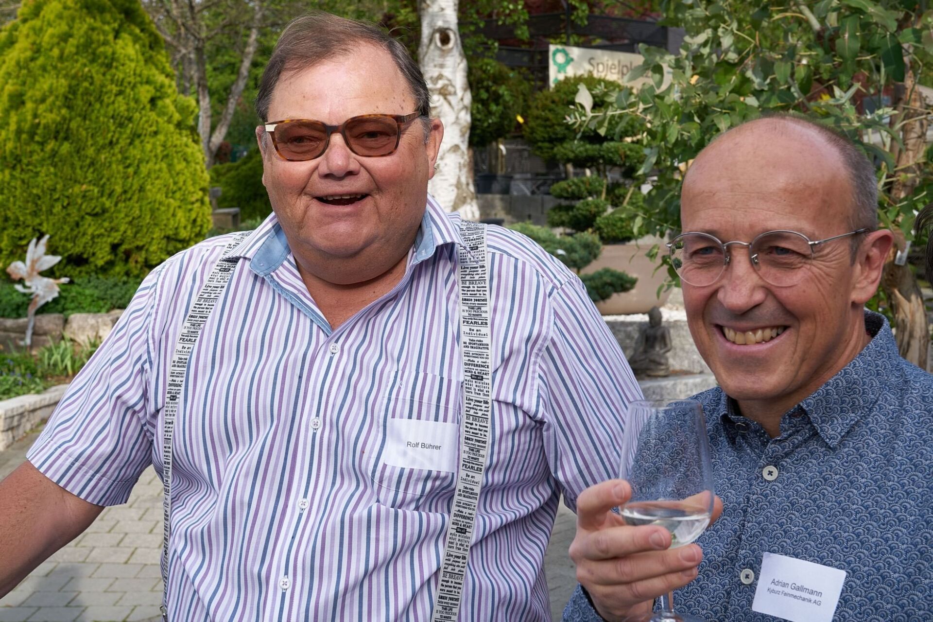 Zwei Männer stehen nebeneinander und einer hält ein Glas Wein.