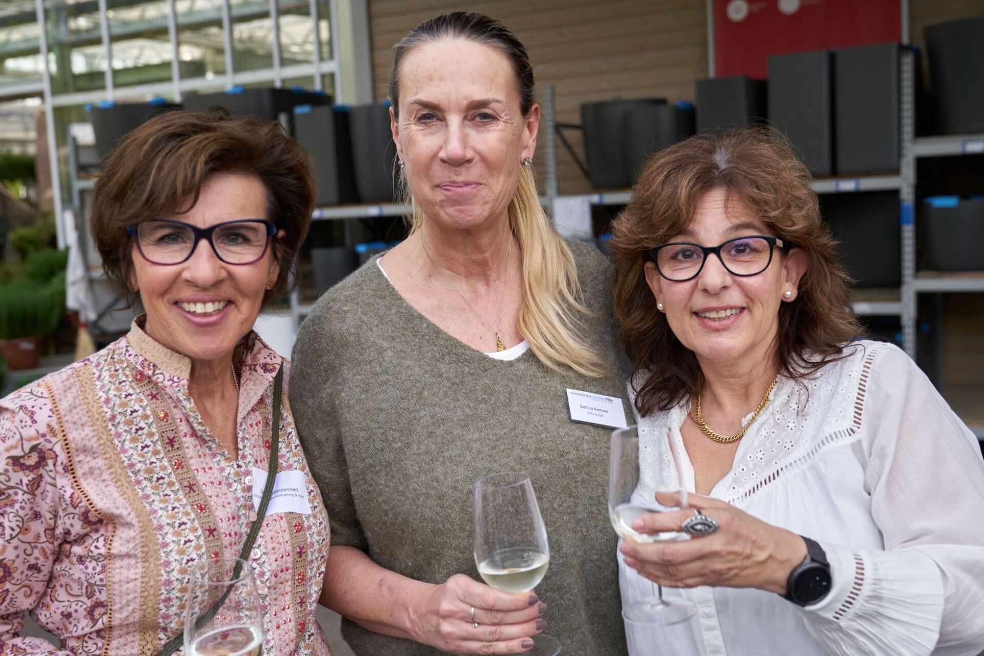 Drei Frauen stehen nebeneinander und halten Weingläser.