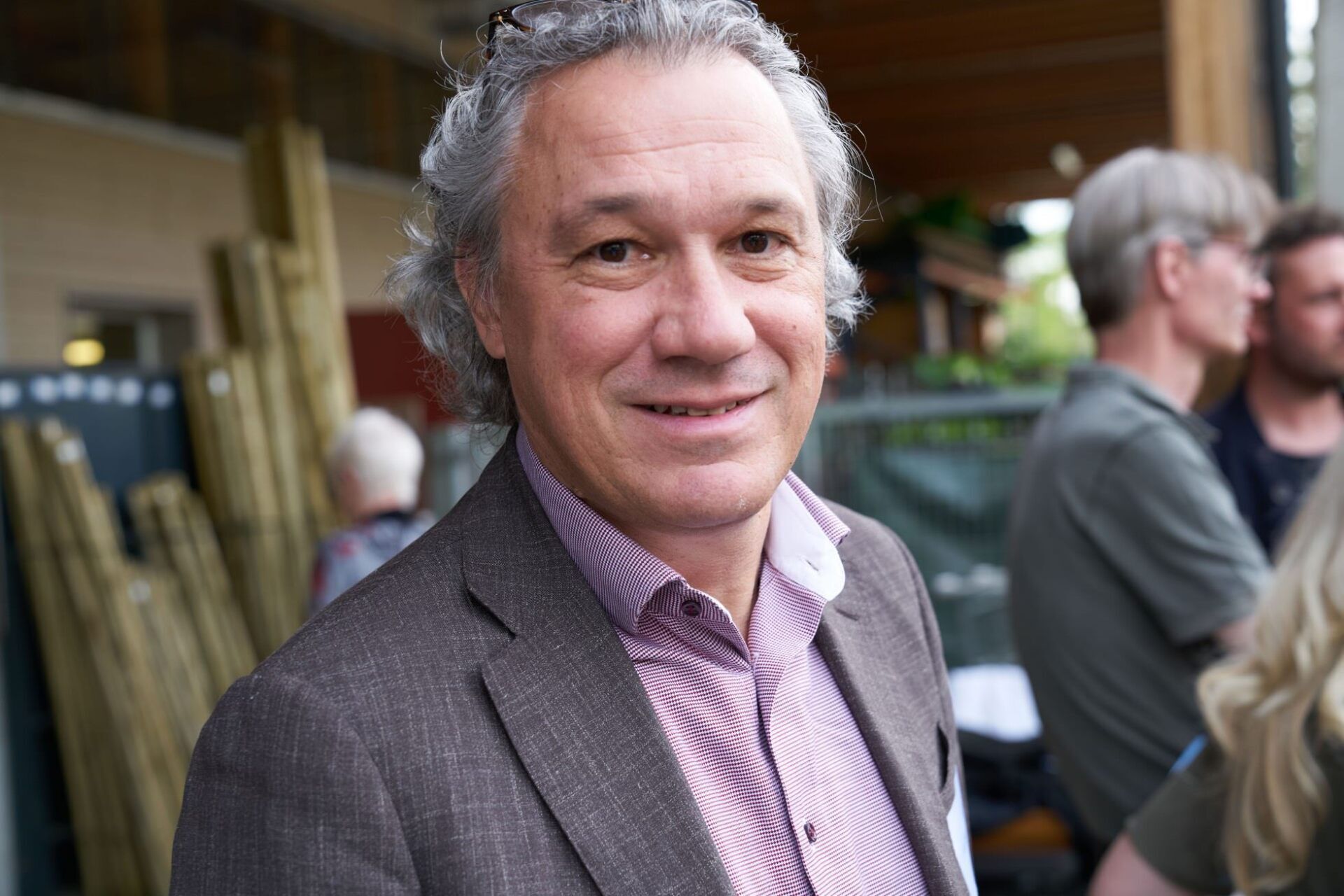 Ein Mann im Anzug lächelt in die Kamera, während er vor einer Gruppe von Menschen steht.