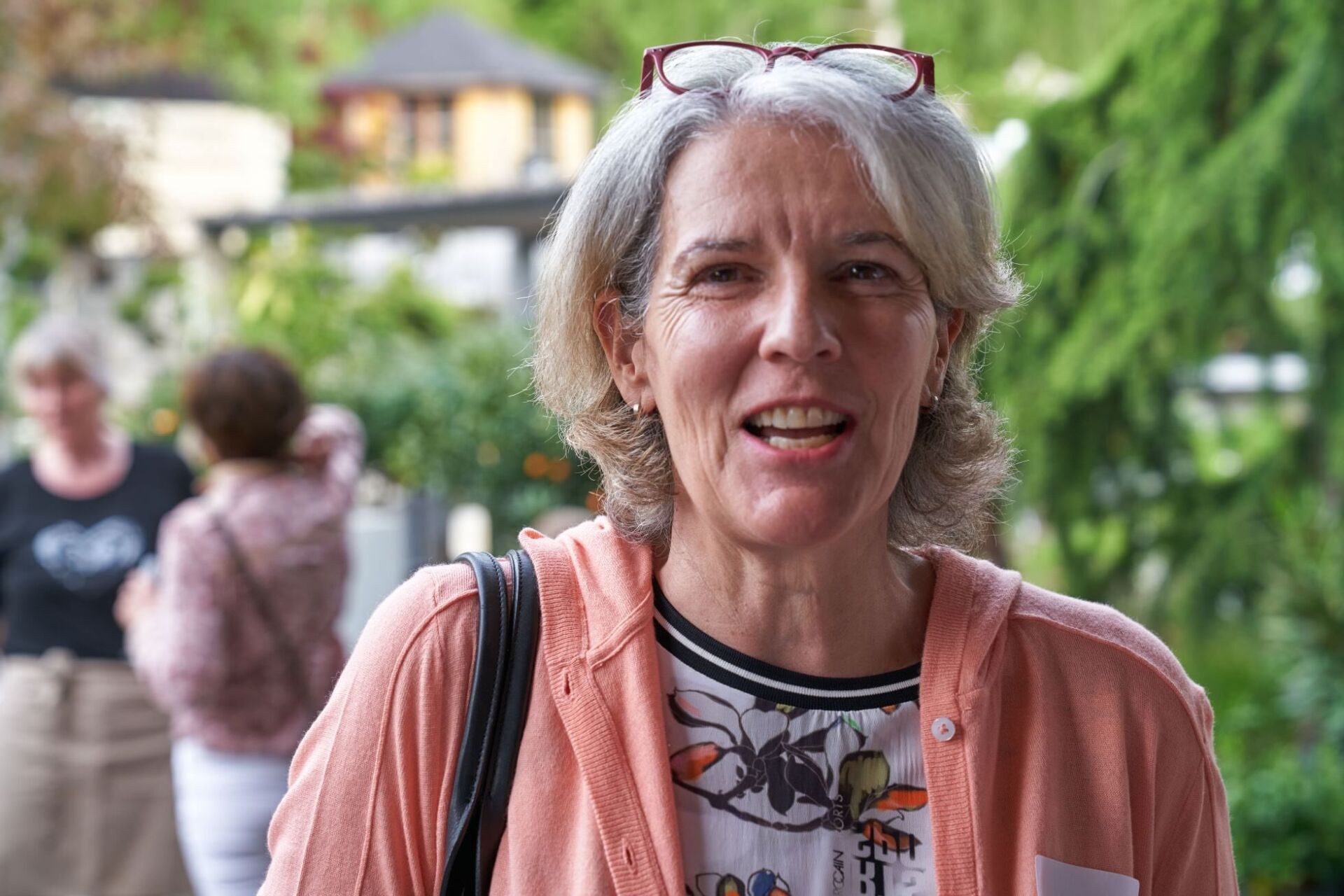 Eine Frau mit Brille und rosa Jacke lächelt.