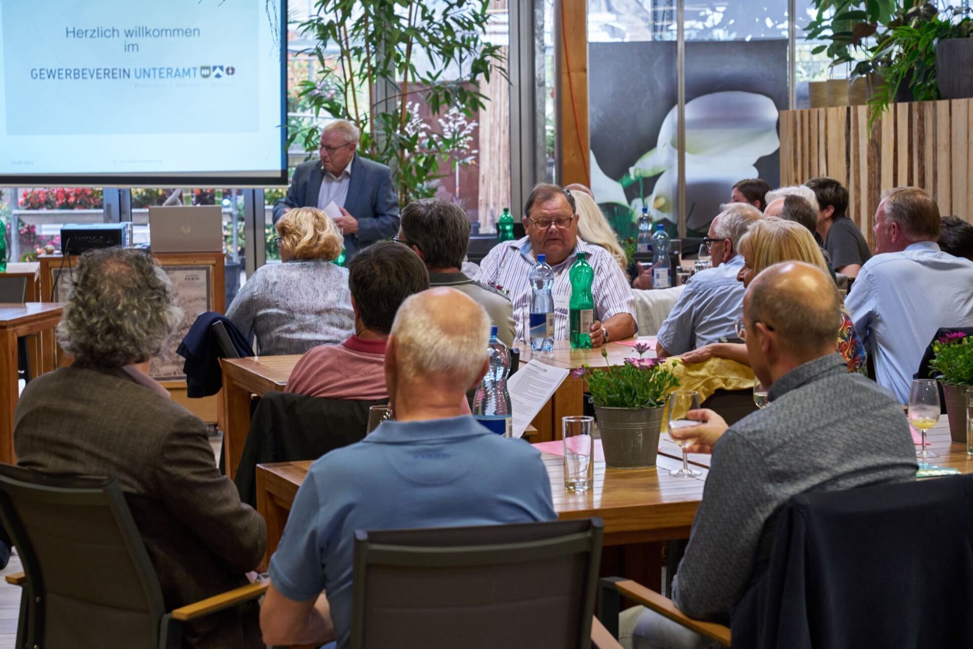 Eine Gruppe von Menschen sitzt an Tischen vor einer Projektionsleinwand.