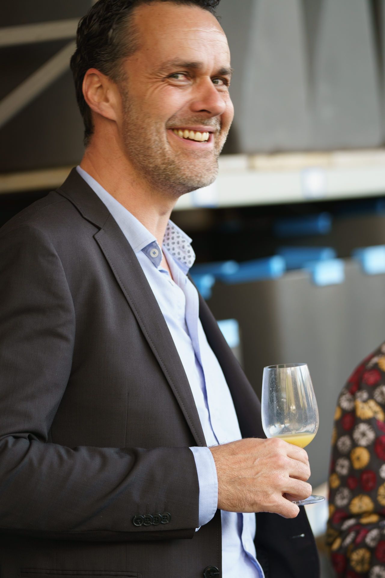 Ein Mann im Anzug hält ein Glas Wein und lächelt.