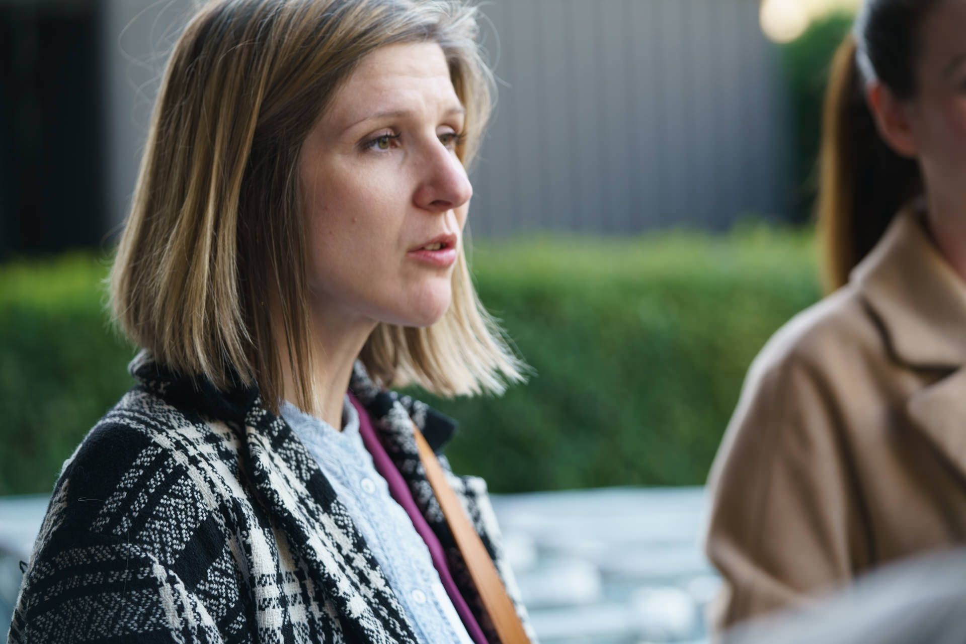 Eine Frau in einem karierten Mantel sitzt neben einer anderen Frau.