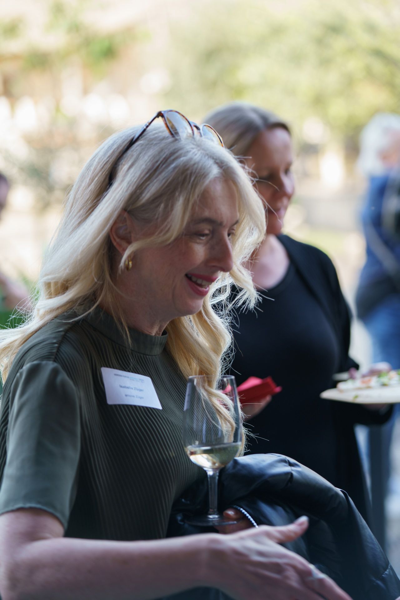 Eine Frau hält ein Glas Wein und lächelt, während sie neben einer anderen Frau steht.
