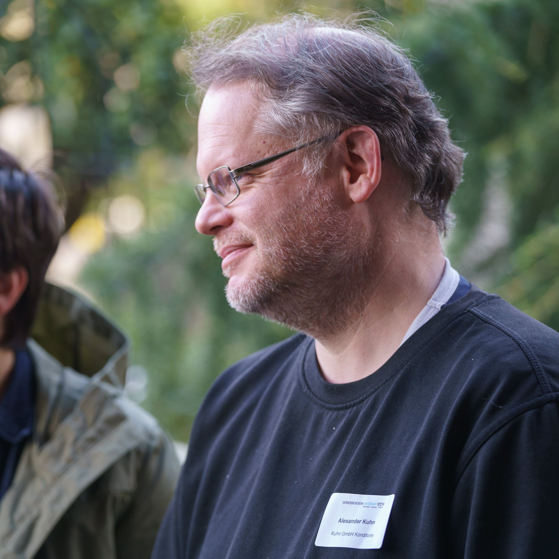 Ein Mann mit Brille und schwarzem Hemd hat ein Namensschild um den Hals