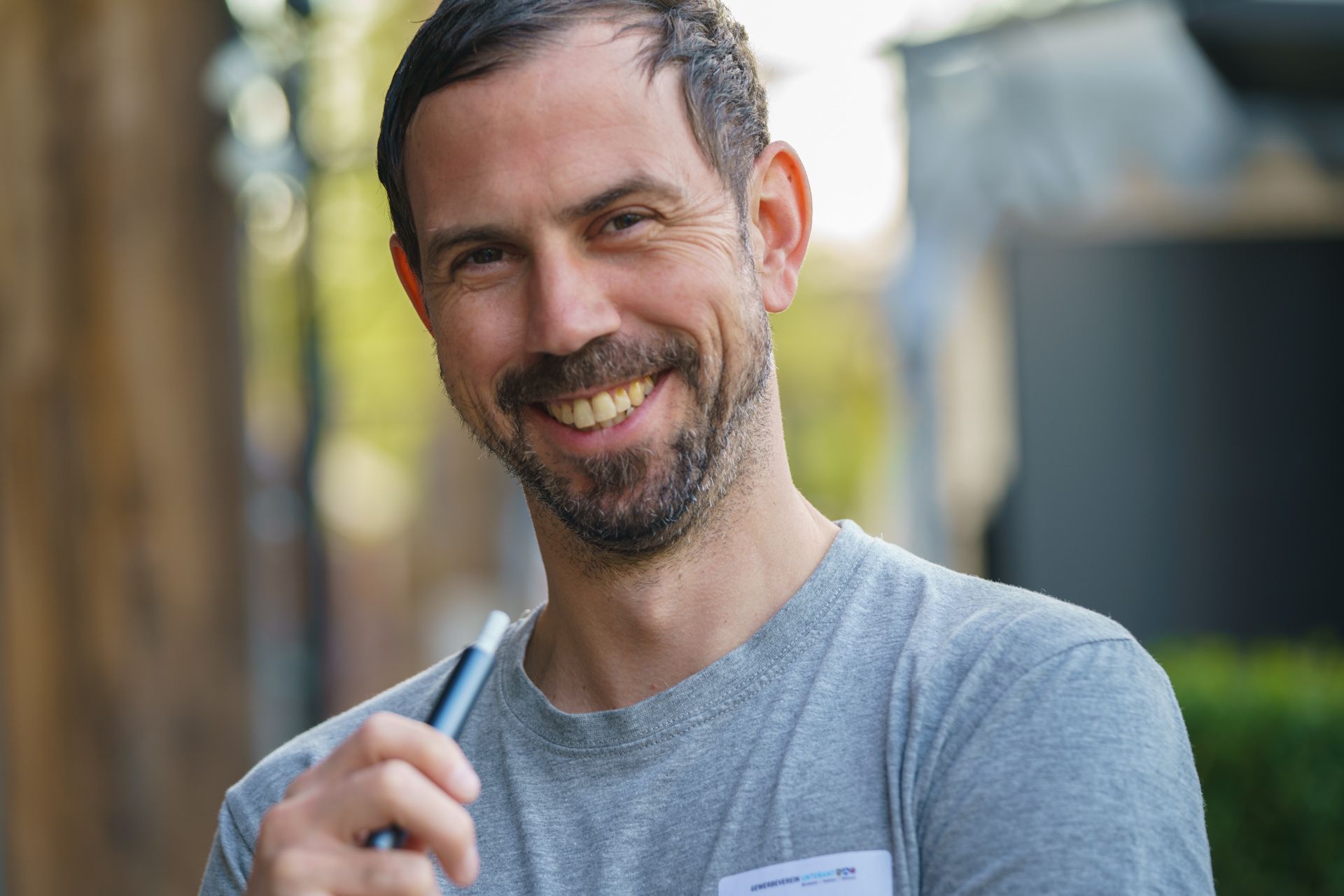 Ein Mann mit Bart hält einen Stift und lächelt.