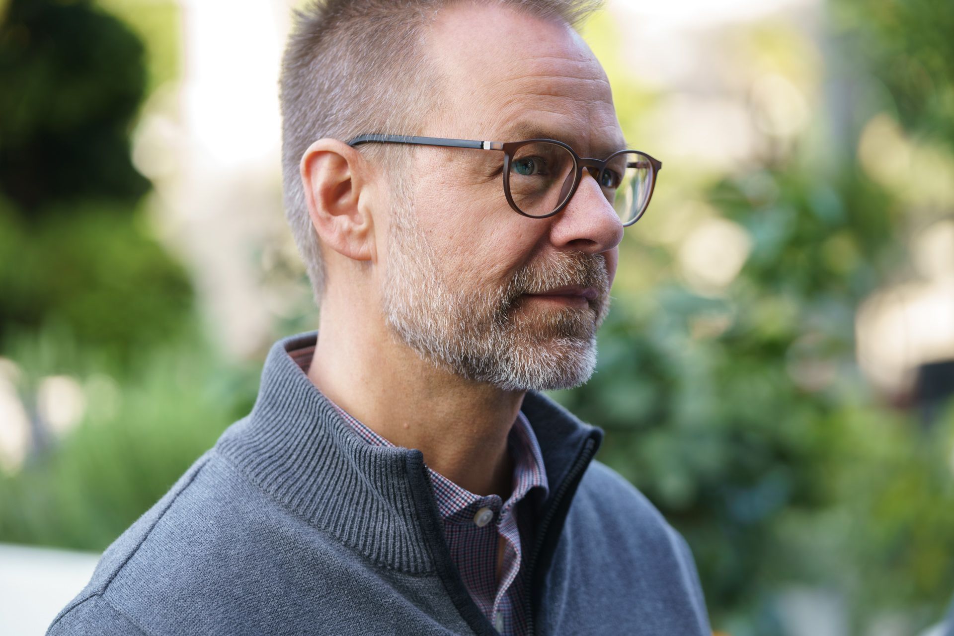 Ein Mann mit Bart und Brille trägt einen grauen Pullover.