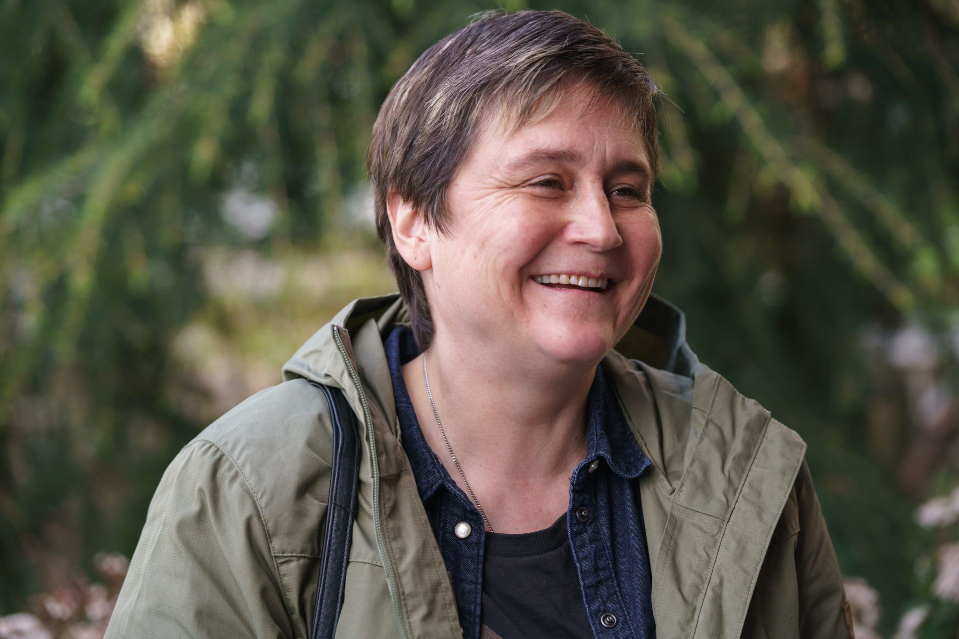 Eine Frau in einer grünen Jacke lächelt vor einem Baum.