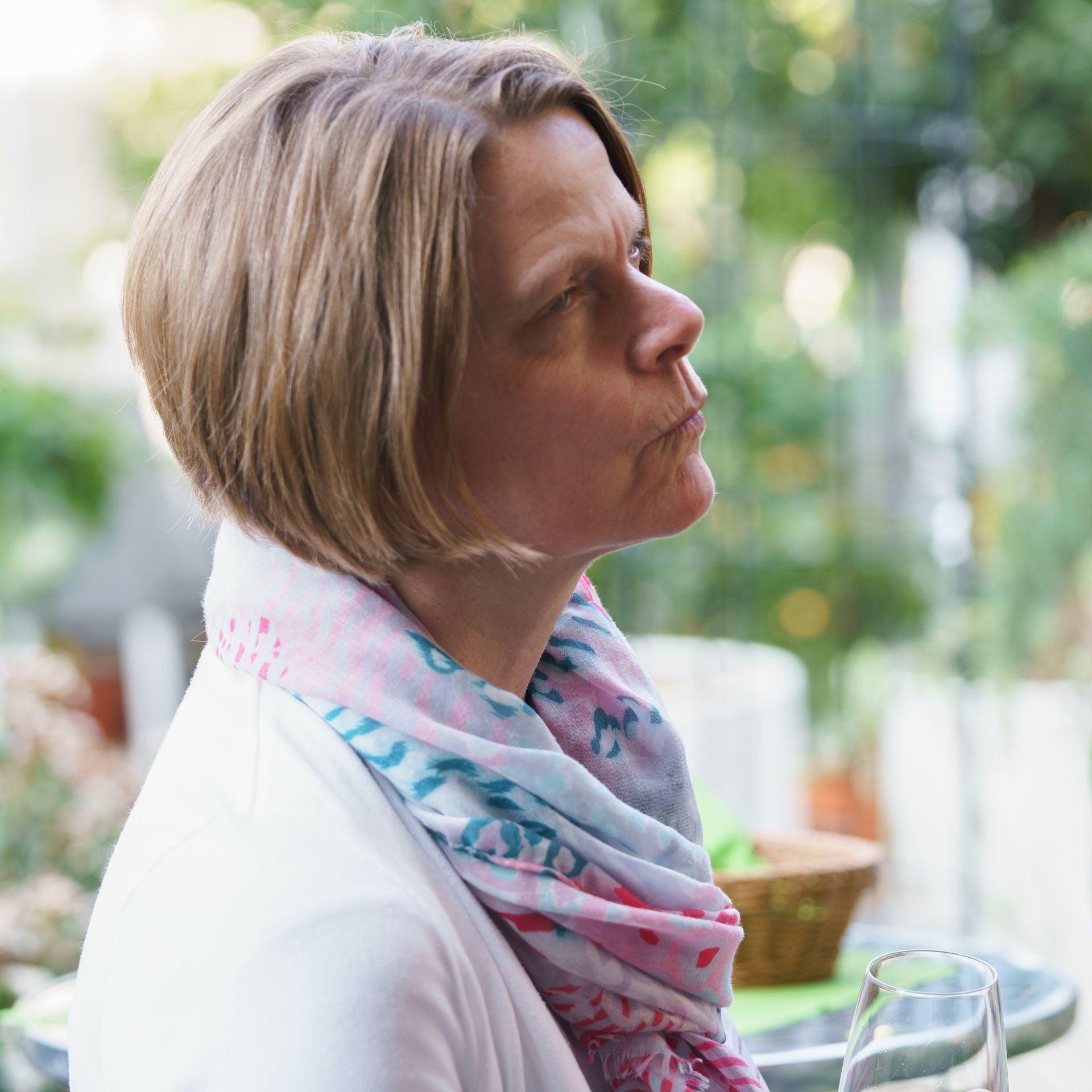 Eine Frau mit einem Schal um den Hals sitzt mit einem Glas Wein an einem Tisch.